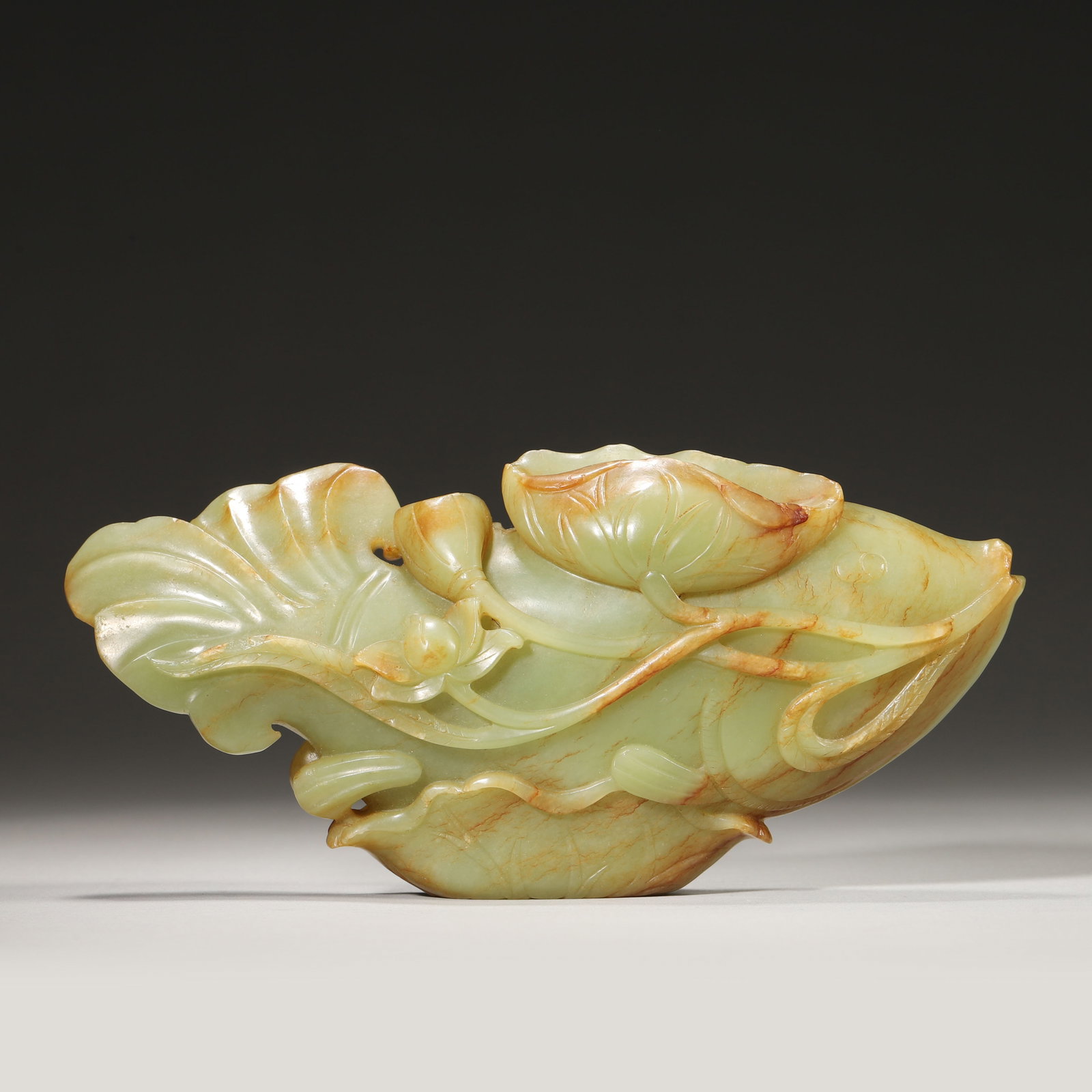 A FINE HETIAN JADE CARVED FISH WITH LOTUS, QING DYNASTY: L: 17cm (6.69in) W: 8cm (3.15in) Weight: 534g (1.18lb)This exquisite Qing Dynasty Hetian jade carving depicts a fish with lotus, symbolizing "surplus year after year". A masterpiece of jade craftsmans
