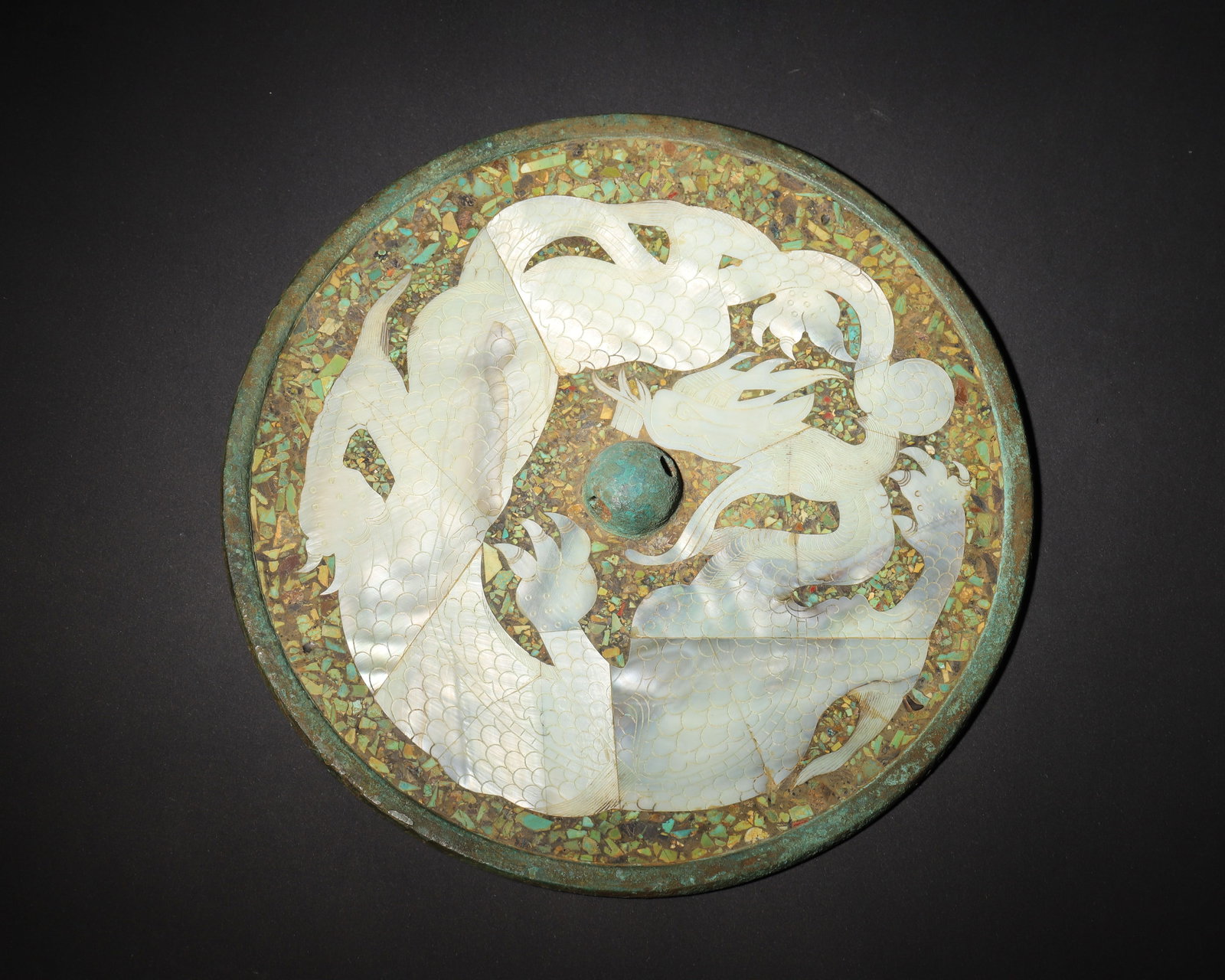 TANG DYNASTY BRONZE MIRROR WITH MOTHER-OF-PEARL & TURQUOISE INLAY, DEPICTING A SINGLE DRAGON CHASING: 7.87in (20.0cm), 2.264lb (1027.0g)A Tang Dynasty bronze mirror featuring a single dragon chasing a pearl, inlaid with iridescent mother-of-pearl and turquoise fragments. The lustrous inlay and dynamic