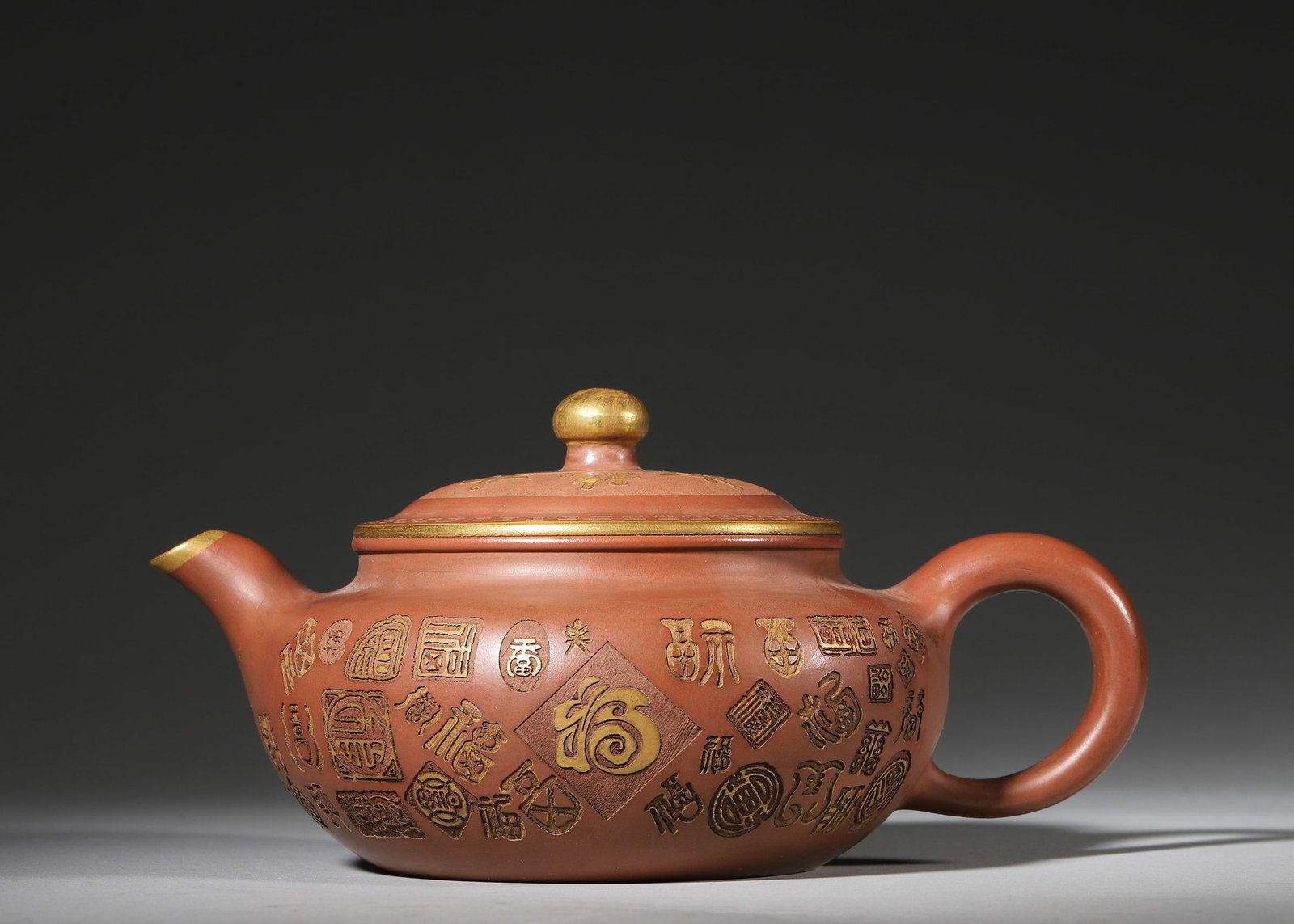 GU JINGZHOU ZISHA TEAPOT WITH GILDED "HUNDRED BLESSINGS" PATTERN: 7.48in x 5.51in x 3.54in (19.0cm x 14.0cm x 9.0cm)This masterpiece was created by Master Gu Jingzhou in the 1980s. Handcrafted from high-grade Yunnan Zisha clay, it features a delicate, warm texture. 