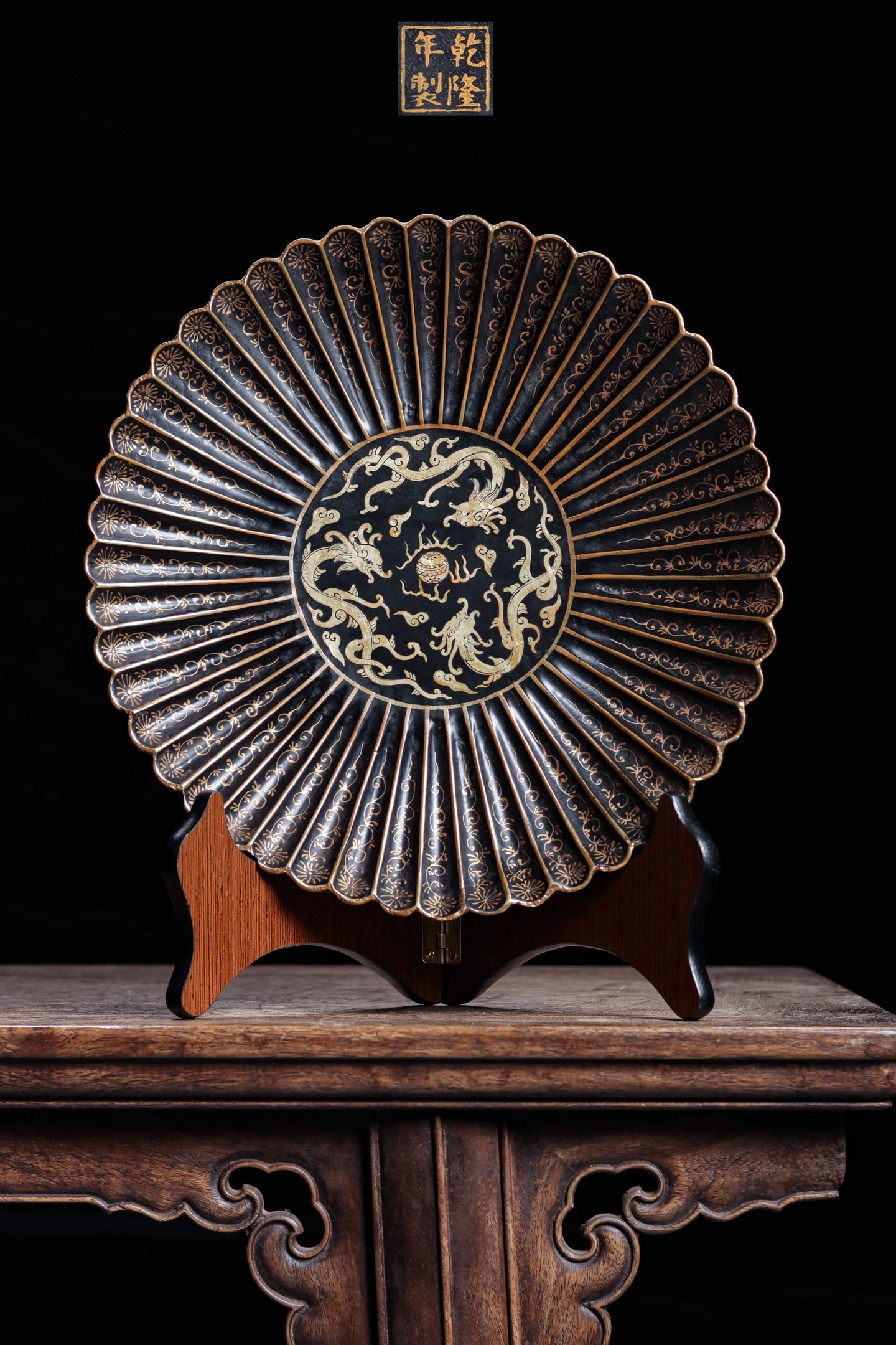 A LARGE GILT-BLACK LACQUER 'DRAGON' CHARGER, MARK AND PERIOD OF QIANLONG: 10.63" x 1.57" (27cm x 4cm)A large Qianlong-marked gilt-black lacquer charger. Chrysanthemum-form with carved wood base, central 'double dragons playing pearl' motif in gold on black lacquer. Fine imp