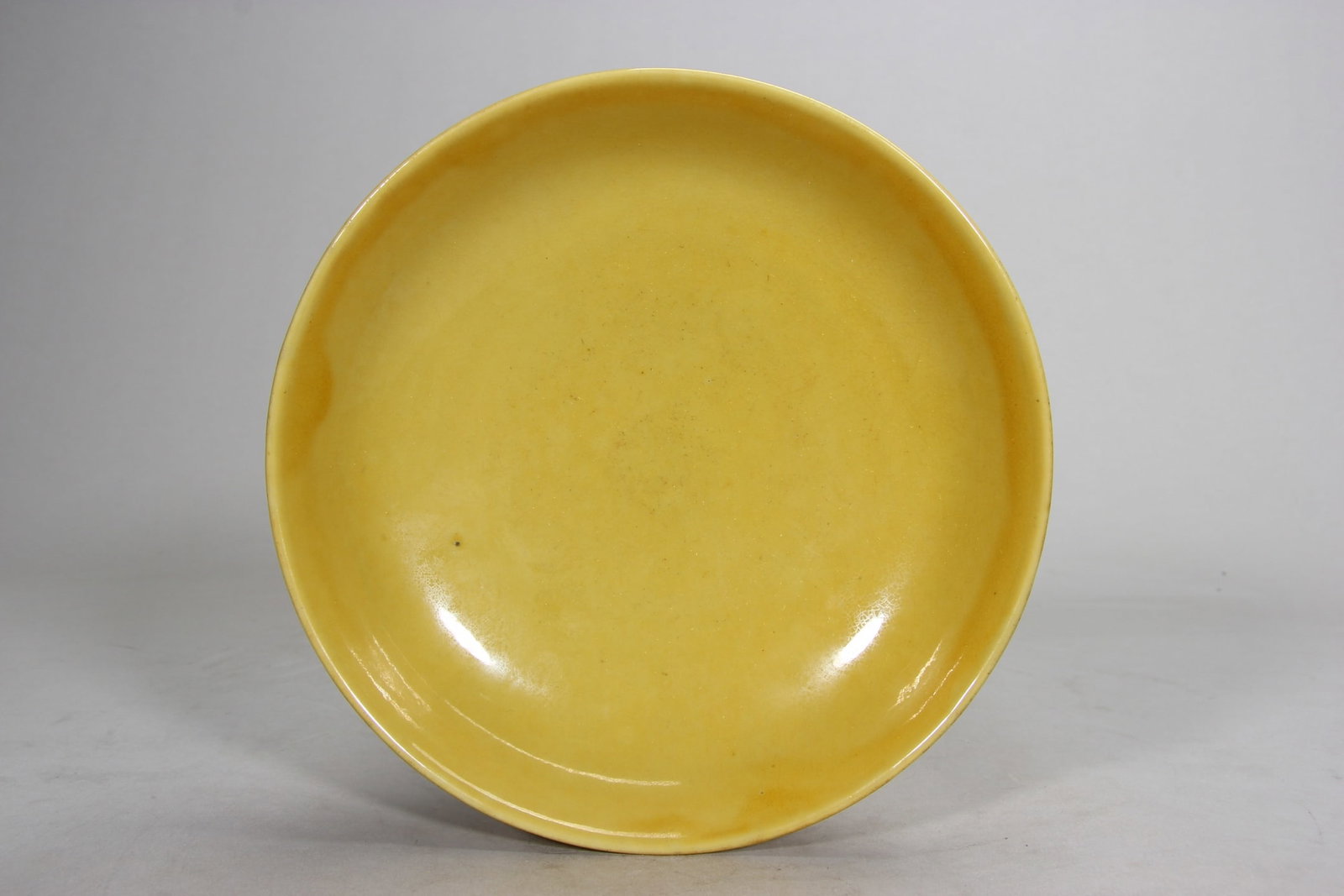 A FINE MING HONGZHI PERIOD IMPERIAL YELLOW GLAZED DISH: D7.05in (D17.9cm)This imperial dish is covered in a rich, lustrous imperial yellow glaze, a hallmark of Hongzhi’s monochrome porcelain. A rare Hongzhi mark example, showcasing exceptional Ming dynas