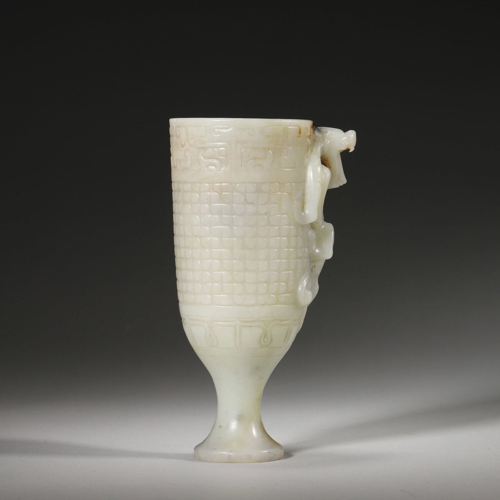 A RARE WHITE JADE TALL STEM CUP WITH CHI-DRAGON HANDLE, HAN DYNASTY: L: 7.5cm (2.95in) W: 5.7cm (2.24in) H: 14cm (5.51in) Weight: 314g (0.69lb)This rare Han Dynasty white jade tall stem cup features a vivid chi-dragon handle and exquisite carvings. A masterpiece of Han