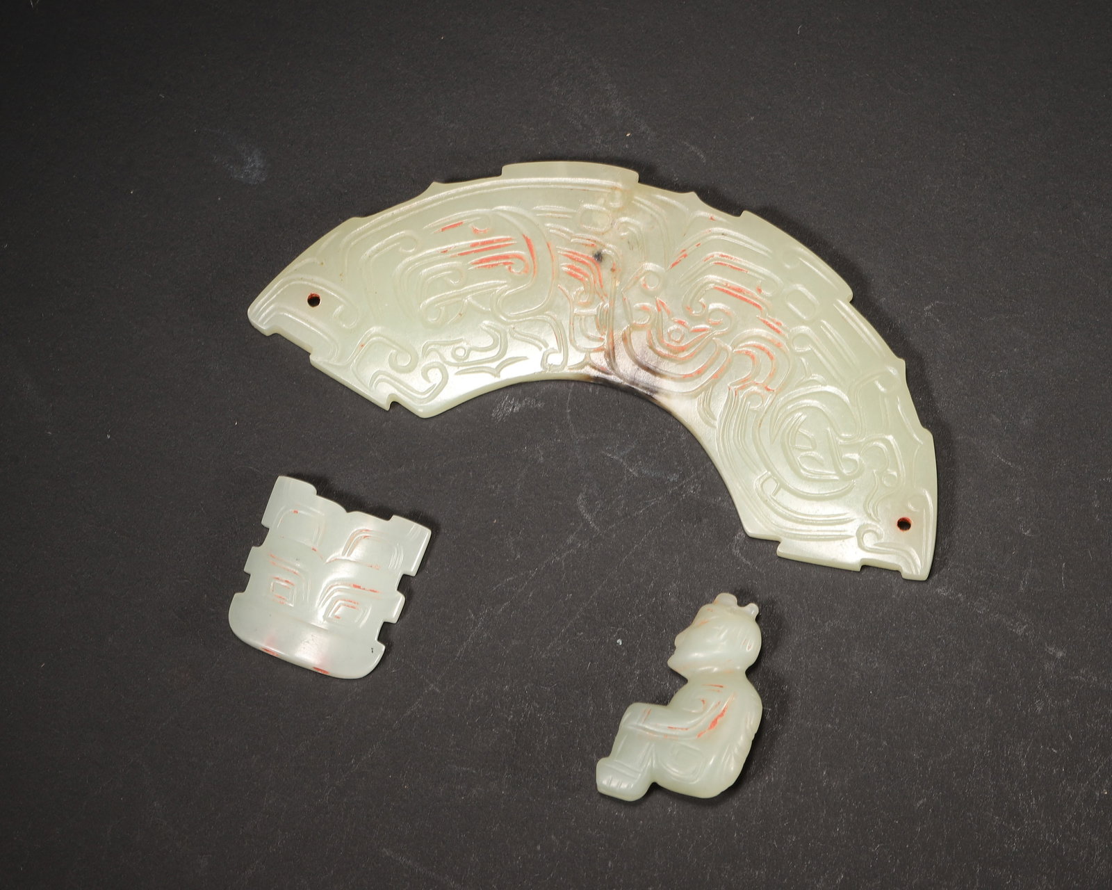 A SET OF THREE JADE HUANG, FIGURE AND BEAST MASK PENDANTS, WESTERN ZHOU DYNASTY: L: 10.5cm (4.13in) W: 4.5cm (1.77in) Weight: 57g (0.13lb)A fine set of three Western Zhou jade pendants, carved with dragon-phoenix, figure and beast mask, archaic style, cinnabar patina, excellent cr