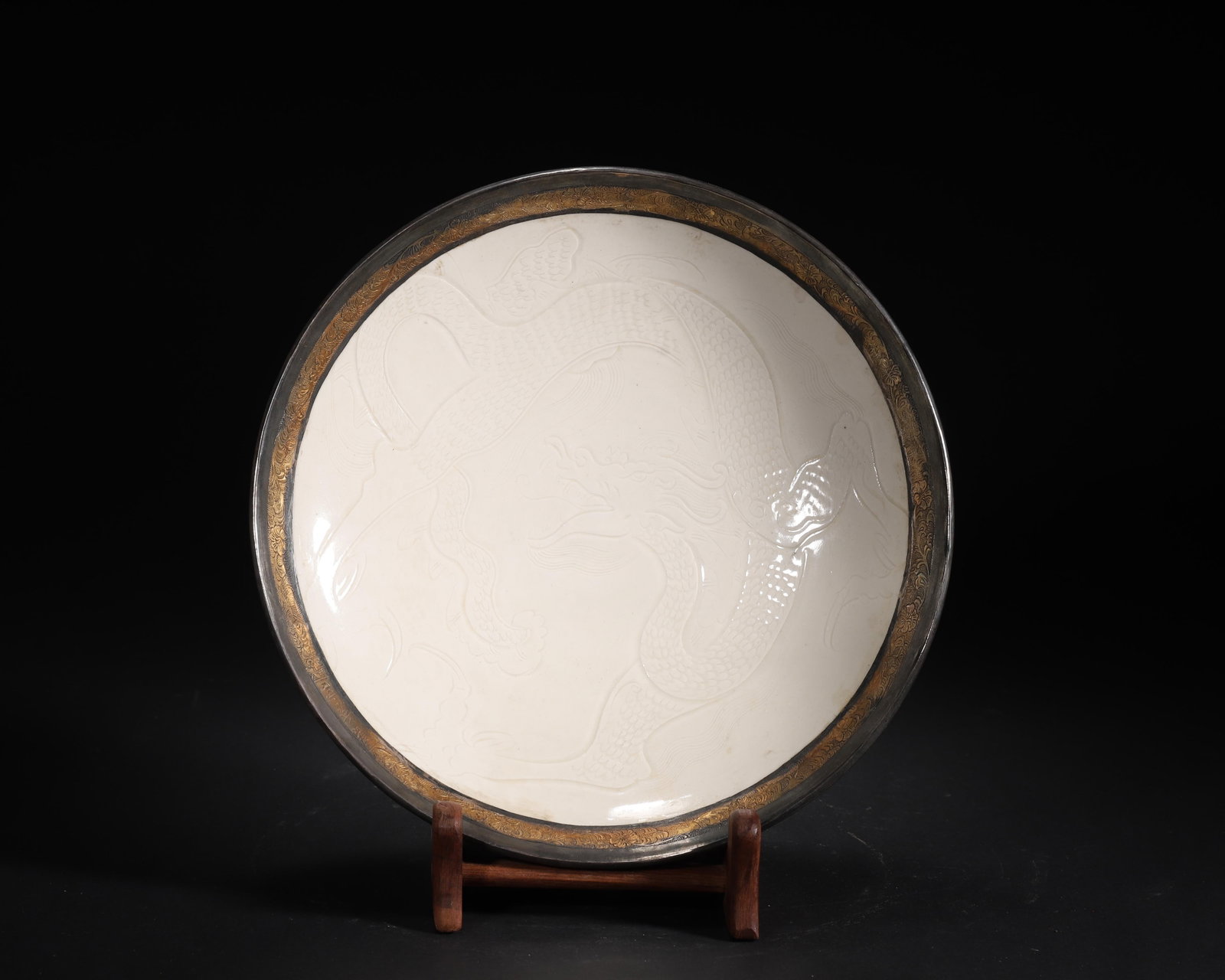 SONG DYNASTY DING KILN WHITE-GLAZED DISH WITH CARVED DRAGON PATTERN (GILDED SILVER-MOUNTED RIM,: 9.06 x 1.97 in (23 x 5 cm)A fine Song Dynasty Ding kiln white-glazed dish, featuring a finely carved dragon pattern. The later gilded silver-mounted rim, inscribed with 'Gui Xiu Gong', bears imperial 