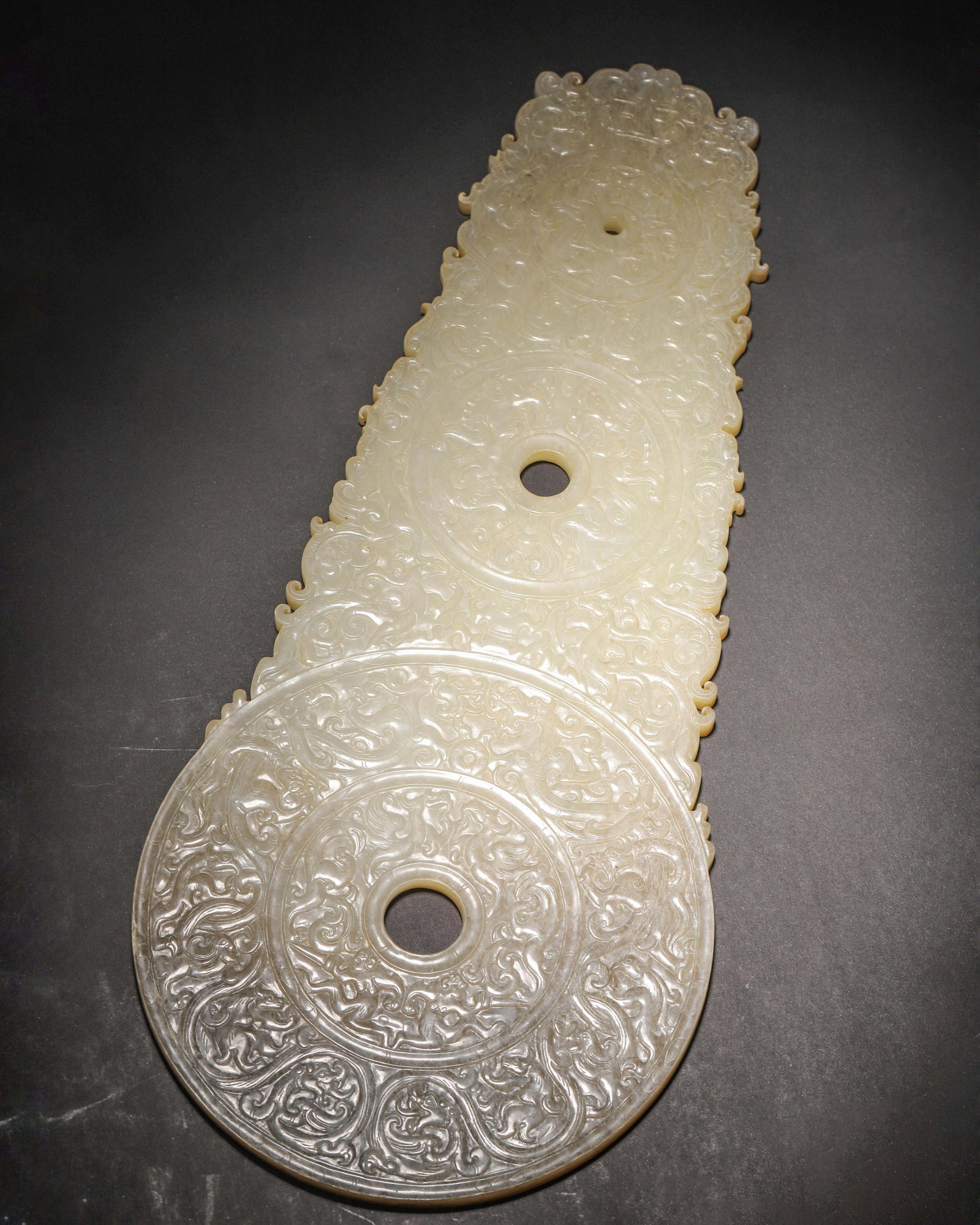 WESTERN HAN DYNASTY HETIAN JADE BI WITH HIGH-RELIEF DRAGON & PHOENIX MOTIFS (TRIPLE-LINKED): 14.57in x 6.3in (37.0cm x 16.0cm) 1.92lb (869.0g)A rare and exceptional Western Han jade piece, crafted from fine Hetian jade. Featuring three linked bi disks exquisitely carved with high-relief drago