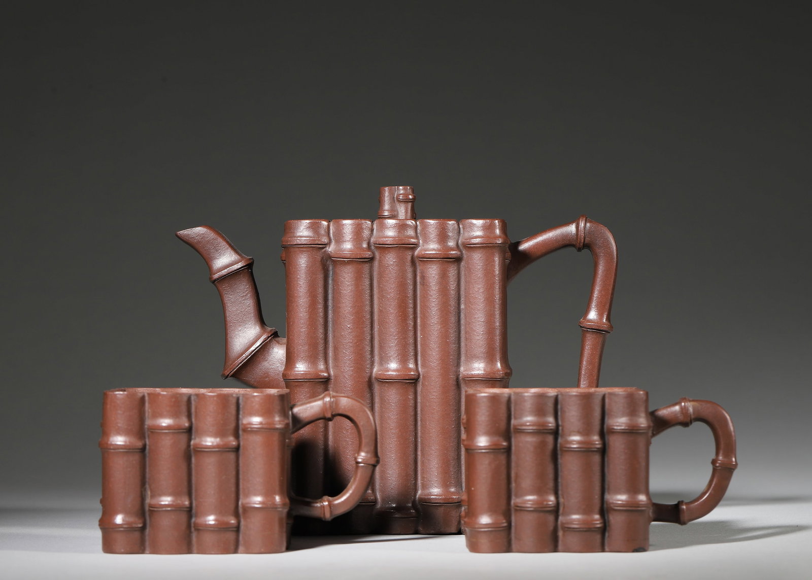 A FINE YIXING ZISHA BAMBOO-FORM TEA SET (POT AND TWO CUPS), MID-QING DYNASTY: 6.1in x 2.95in x 4.72in (15.5cm x 7.5cm x 12.0cm)This elegant tea set is crafted from fine Yixing zisha clay, featuring a teapot and two cups modeled as bundled bamboo stalks. The detailed bamboo join