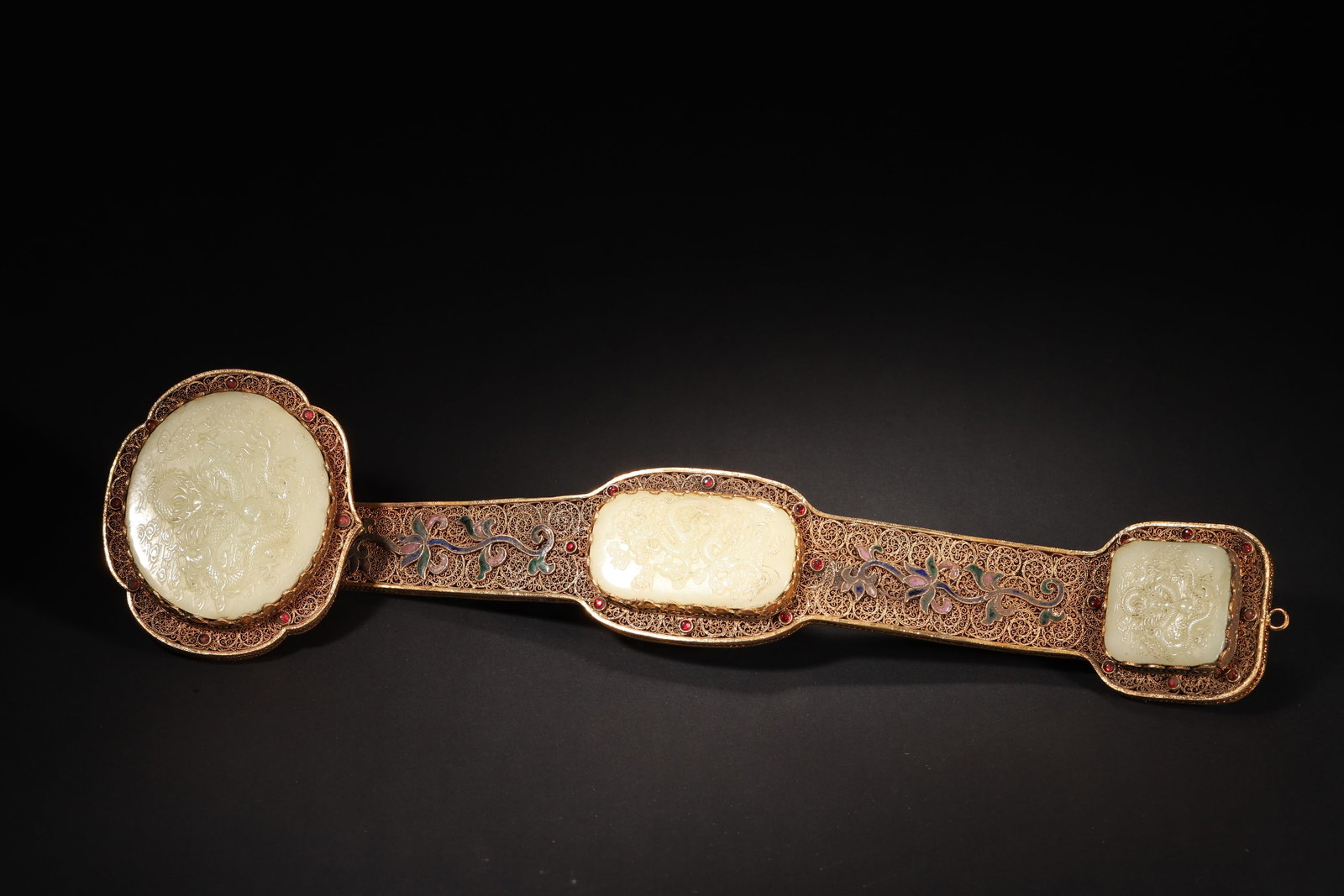 A FINE IMPERIAL GILT-SILVER FILIGREE AND ENAMEL RUYI SCEPTRE WITH INLAID JADE DRAGON PANELS,: 17.32in x 4.33in (44.0cm x 11.0cm), 1.803lb (818.0g)This imperial ruyi sceptre, crafted in the Qianlong period, features gilt-silver filigree, enamel, ruby inlays, and three jade panels carved with fi