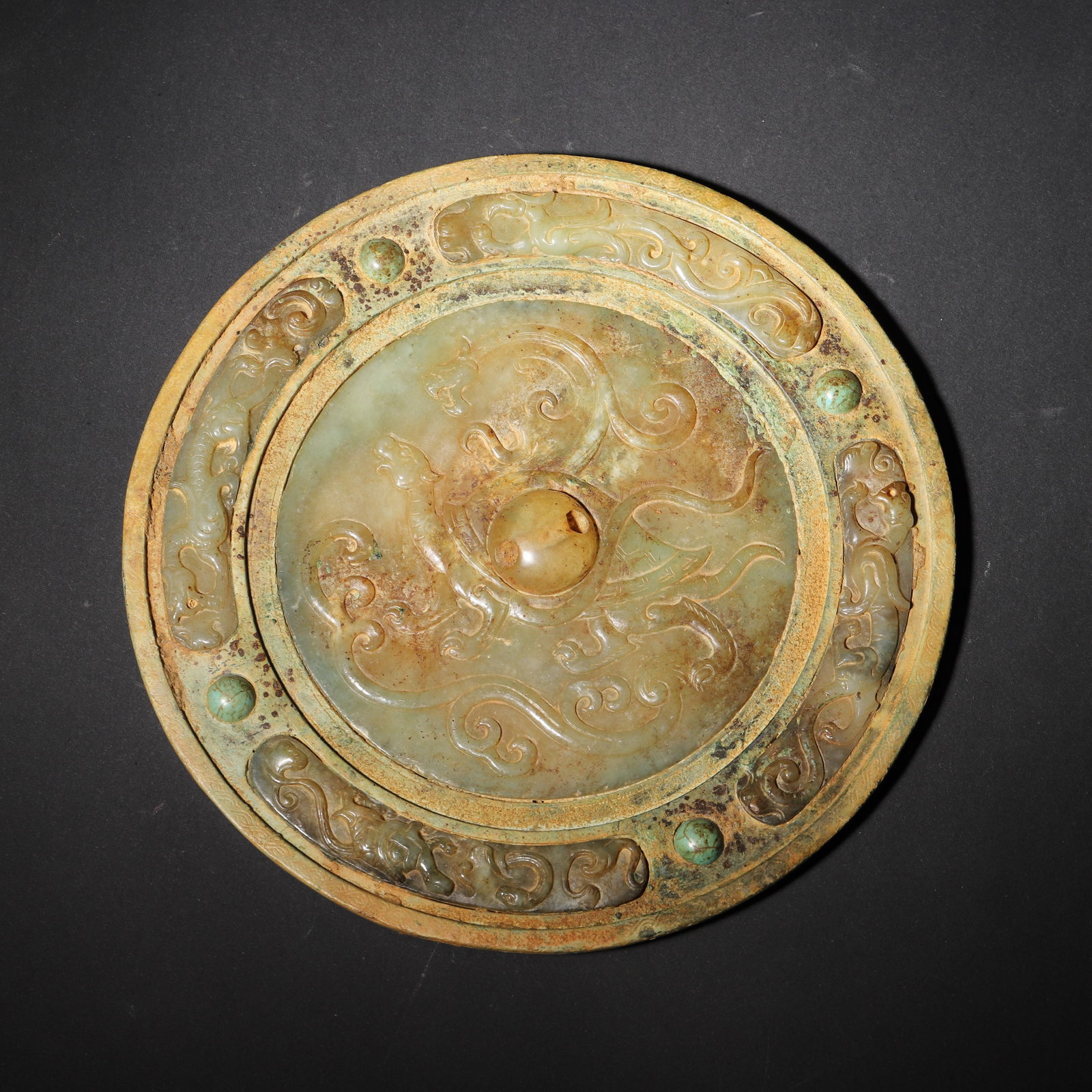 TANG DYNASTY BRONZE-MOUNTED JADE MIRROR WITH TURQUOISE INLAY, DEPICTING THE XUANWU (TURTLE-SNAKE): 6.69in (17.0cm), 1.638lb (743.0g)A rare Tang Dynasty mirror with a bronze frame, inlaid jade center carved with the Xuanwu (turtle-snake) motif, and turquoise accents. It exemplifies exquisite Tang cr