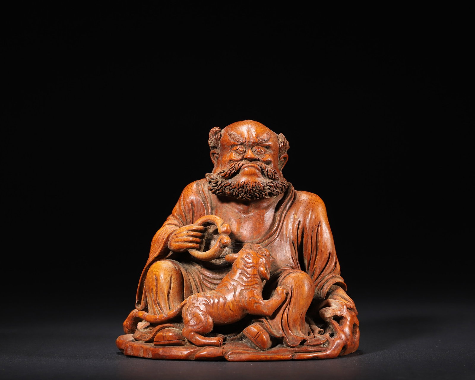 MID-QING DYNASTY, A BAMBOO ROOT CARVING OF LUOHAN SUBDUING A TIGER: 4.92in x 4.72in x 4.92in (12.5cm x 12.0cm x 12.5cm), 0.511lb (232.0g)This Mid-Qing bamboo root carving depicts Luohan subduing a tiger. Carved from natural bamboo root, it features a majestic Luohan w