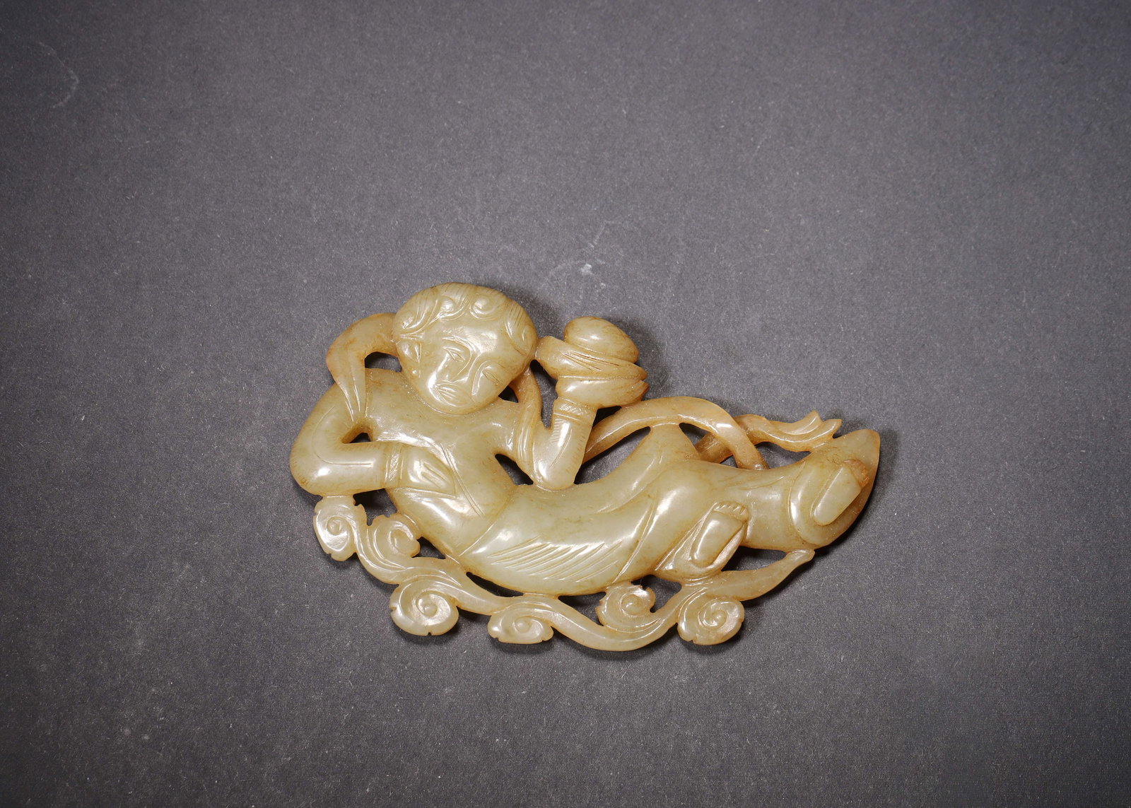MING DYNASTY GREENISH YELLOW JADE OPENWORK FLYING APSARAS OFFERING TREASURE PENDANT: 3.62in x 2.24in (9.2cm x 5.7cm) 0.143lbs (65g)A fine Ming Dynasty greenish yellow jade openwork pendant, depicting a flying apsaras offering a treasure box, with flowing ribbons and scrolling clouds. 