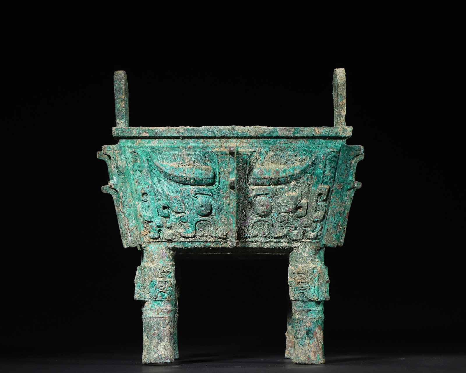 WESTERN ZHOU DYNASTY BRONZE SQUARE DING VESSEL WITH TAOTIE MASKS: 7.48in x 9.45in (19.0cm x 24.0cm), 8.02lb (3638.0g)A fine Western Zhou bronze square ding vessel, with symmetric taotie masks on the body, cloud-patterned ground, and four pillar legs. Exemplifying an