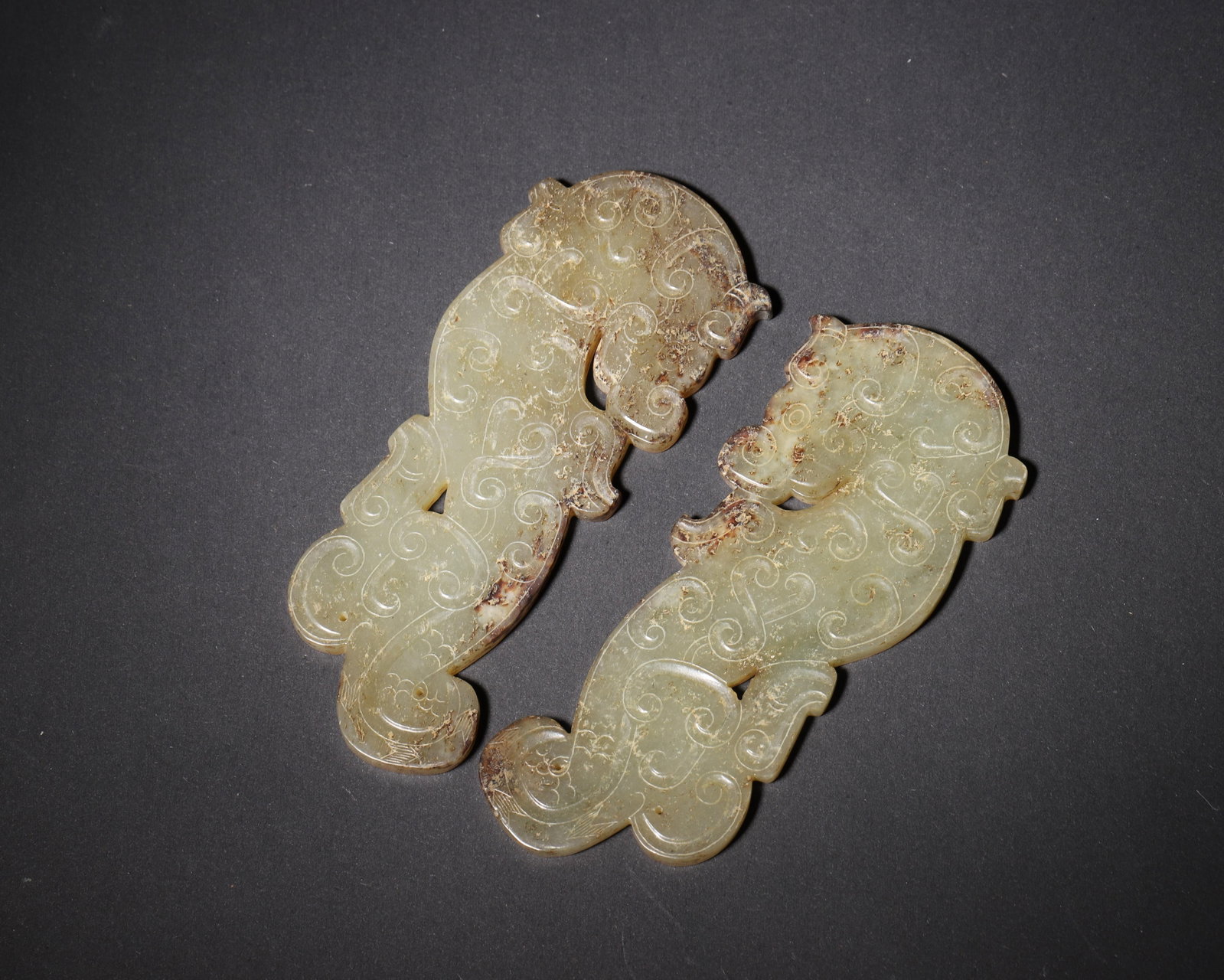 HAN DYNASTY, A PAIR OF BLUISH-WHITE JADE S-SHAPED CHI DRAGON PENDANTS WITH CLOUD SCROLL PATTERNS: 4.33in x 1.89in (11.0cm x 4.8cm), 0.249lb (113.0g)Crafted of fine bluish?white jade, this paired Han S?shaped chi dragon pendants feature fluent cloud scrolls carved in classic slender-line technique.