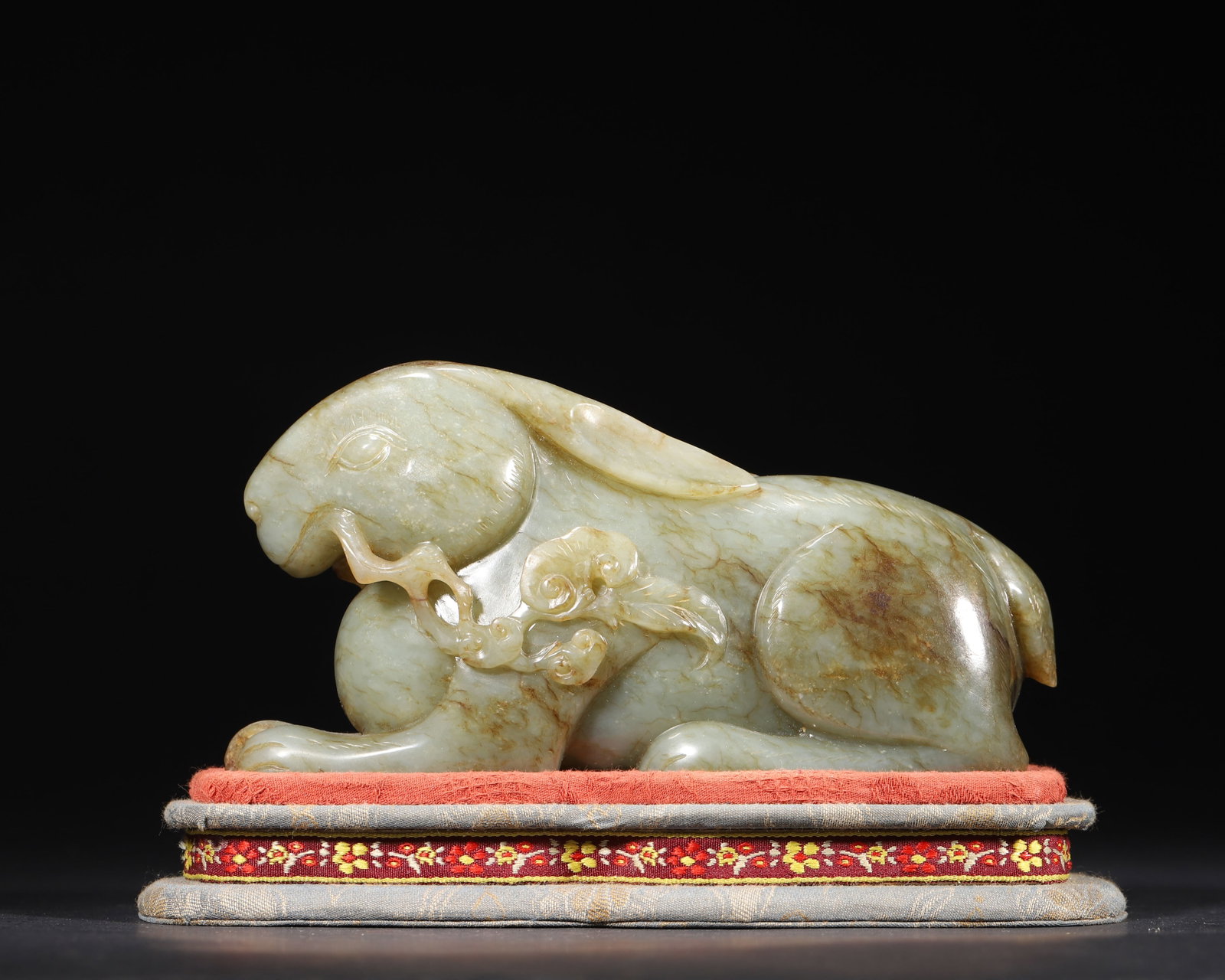 A FINE HETIAN GREEN JADE CARVING OF A RABBIT HOLDING LINGZHI, MID-QING DYNASTY: 6.3in x 2.36in x 3.54in (16.0cm x 6.0cm x 9.0cm), 2.734lb (1240.0g)This well-carved Mid-Qing Hetian green jade recumbent rabbit holds a lingzhi sprig in its mouth, with natural hairline inclusions. It