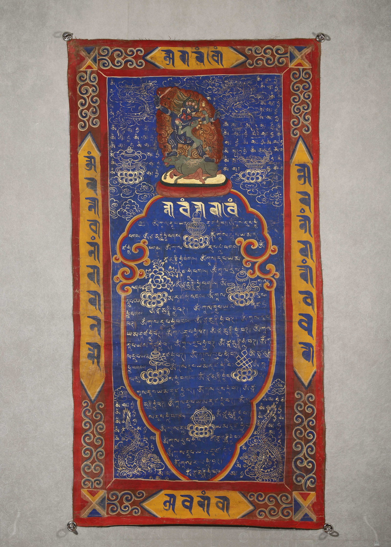 TIBETAN SUTRA THANGKA WITH CINNABAR HANDPRINT, 19TH CENTURY: 49.21in x 25.59in (125.0cm x 65.0cm)This 19th-century Tibetan Buddhist Sutra Thangka, a sacred ritual artifact, features deep sapphire background with exquisitely gilded Tibetan scriptures and guardia