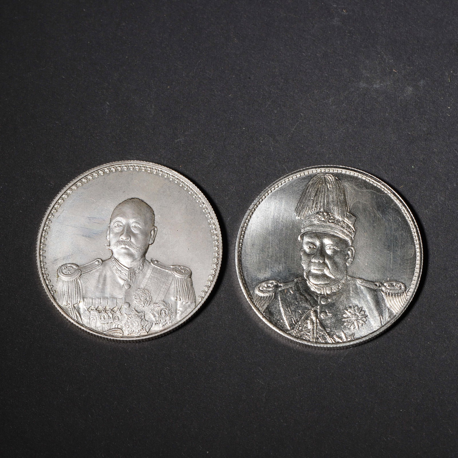 SET OF TWO YUAN SHIKAI COMMEMORATIVE SILVER COINS,Republic of China: 1.57in (4.0cm) 0.121lbs (55g)This set of two silver coins features bright luster and pristine condition. One displays Yuan Shikai in military attire with medals, reverse with crossed flags; the other 
