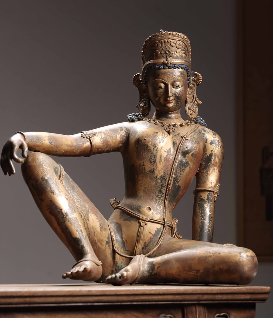 A GILT-BRONZE FIGURE OF BUDDHA NEPAL, MALLA PERIOD, 14TH CENTURY: 22.83" x 22.05" x 11.81" (58cm x 56cm x 30cm) 45.08lb (20450g)This gilt-bronze Buddha statue, crafted in Nepal's Malla Dynasty era, features a serene expression with downcast eyes and a gentle smile. 