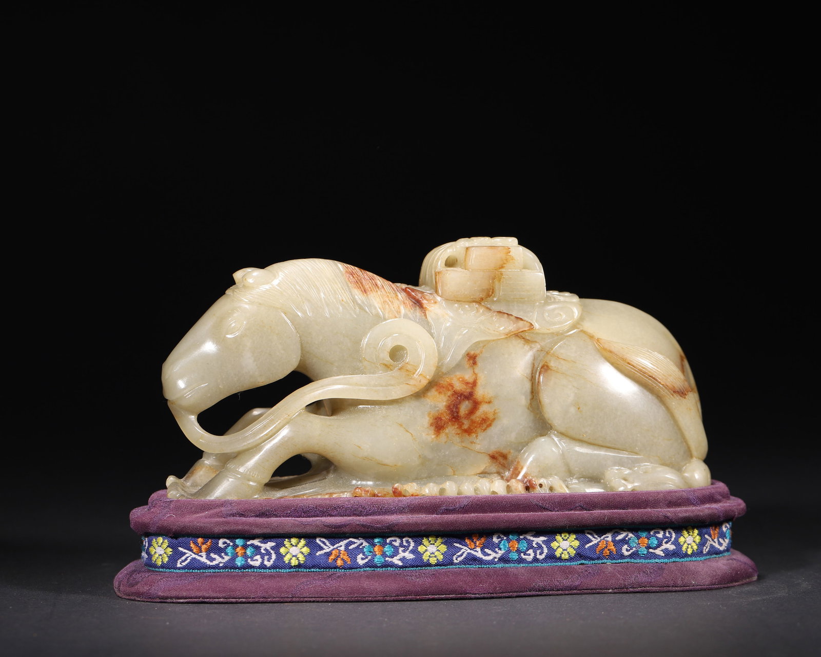 A FINE HETIAN GREEN JADE 'HORSE CARRYING SEAL' ORNAMENT, MID-QING DYNASTY (WITH ORIGINAL STAND): 6.69in x 2.36in x 3.15in (17.0cm x 6.0cm x 8.0cm), 2.421lb (1098.0g)This well-carved Mid-Qing Hetian green jade ornament depicts a recumbent horse carrying a seal box, with natural russet inclusions. 