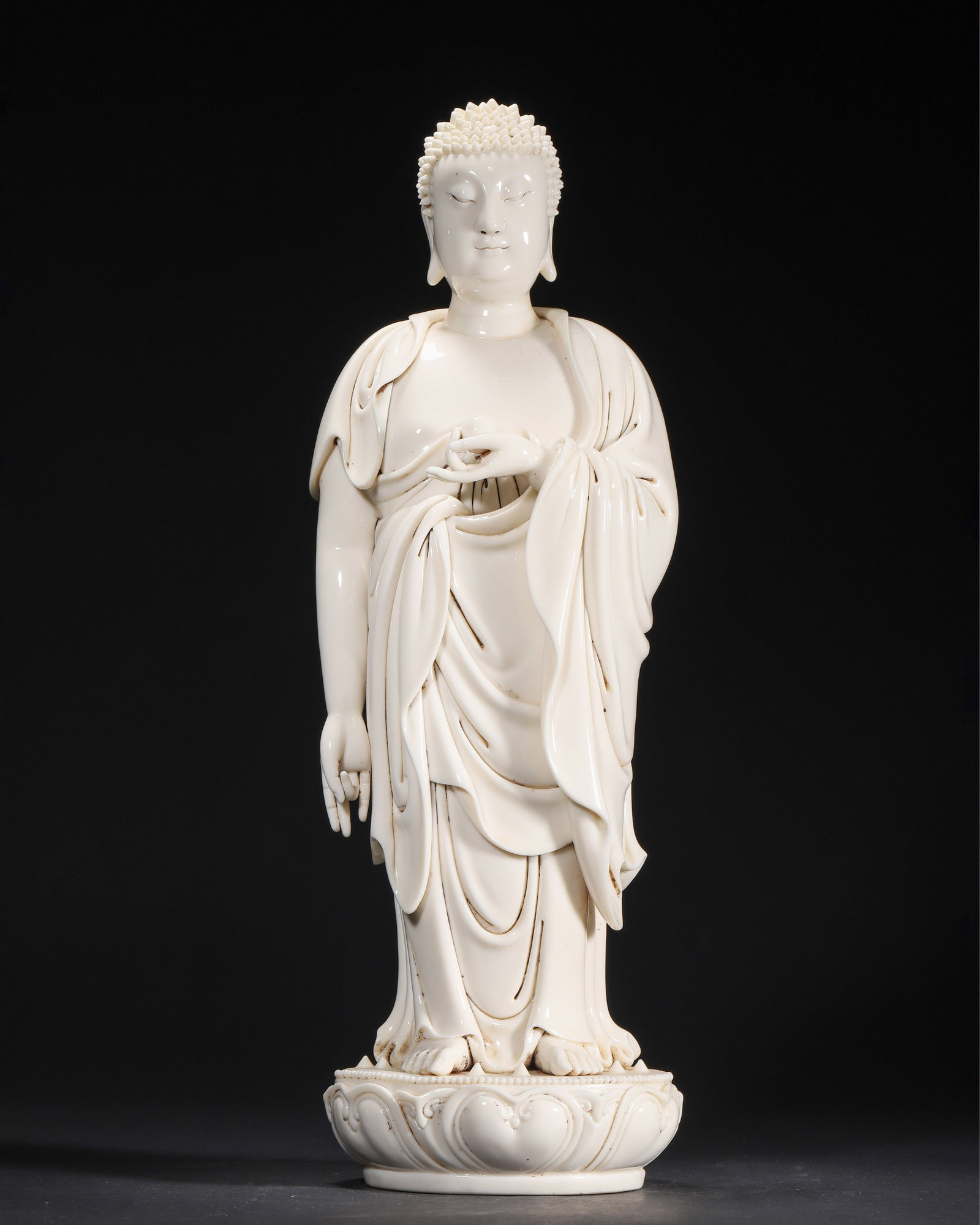 QING DYNASTY, A DEHUA WHITE-GLAZED STANDING FIGURE OF AMITABHA BUDDHA, WITH SEAL MARK: 5.51" x 4.72" x 8.27" (14.0cm x 12.0cm x 21.0cm)This Dehua porcelain figure of Amitabha Buddha is covered in a creamy ivory glaze. It features flowing robes, a compassionate face, and a seal mark on t