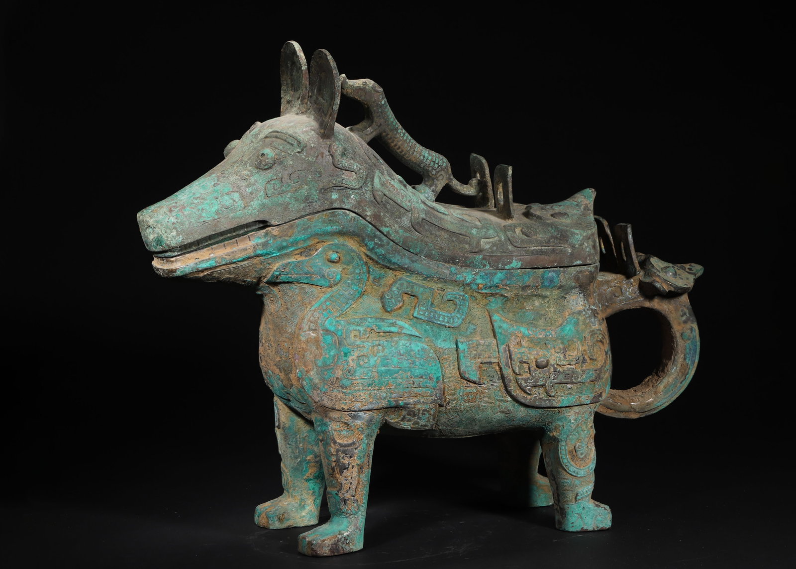 LATE SHANG DYNASTY BRONZE ANIMAL-FORM GONG VESSEL WITH COVER AND INSCRIPTIONS: 21.65in x 6.3in x 17.72in (55.0cm x 16.0cm x 45.0cm), 39.683lb (18000.0g)This Late Shang bronze gong is shaped like a mythical beast, with a climbing dragon finial on its lid. High-relief beast masks,