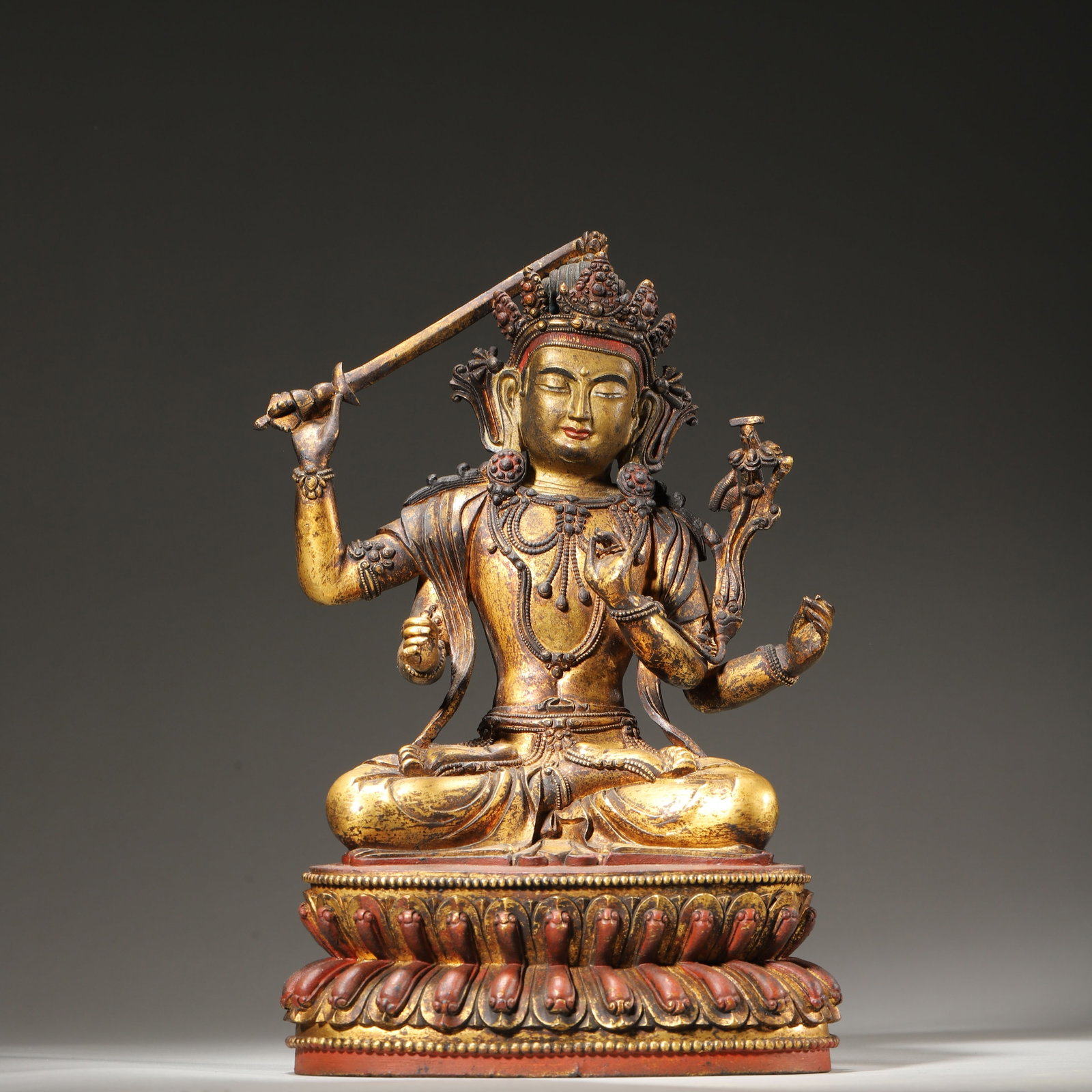 A GILT-BRONZE FOUR-ARMED MANJUSHRI STATUE, QING DYNASTY (18TH-19TH CENTURY): 6.69in x 4.33in x 9.84in (17.0cm x 11.0cm x 25.0cm) 7.33lb (3327.0g)This exquisite Qing Dynasty gilt-bronze Four-Armed Manjushri statue is finely cast with a serene expression, holding a wisdom sword 