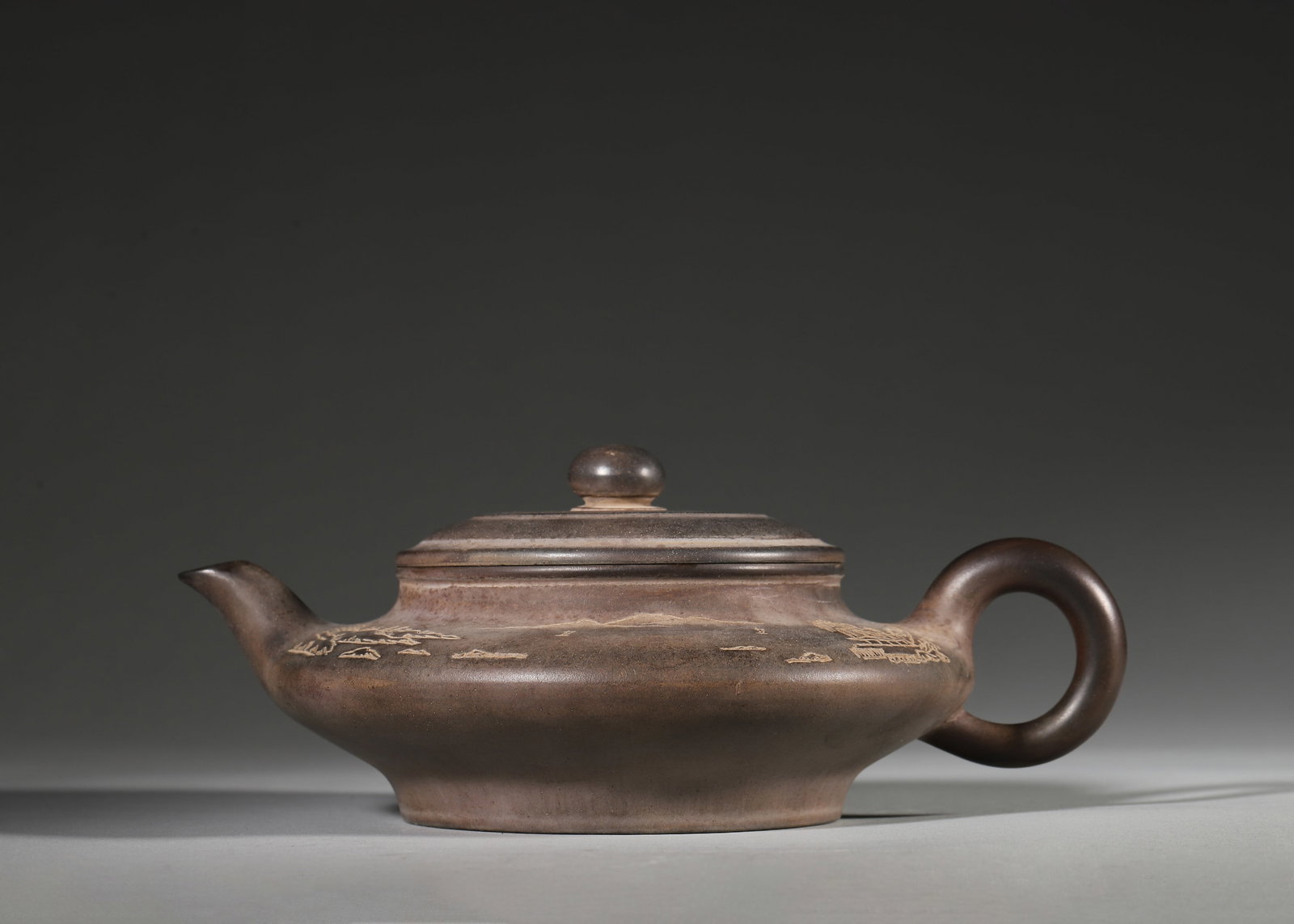MODERN ZISHA TEAPOT WITH LANDSCAPE PAINTING BY GU JINGZHOU (1943): 8.27in x 5.91in x 2.76in (21.0cm x 15.0cm x 7.0cm)Crafted by master Gu Jingzhou in 1943, this flat-shaped Zisha teapot features delicate landscape painting on dark brown clay. It embodies the literati
