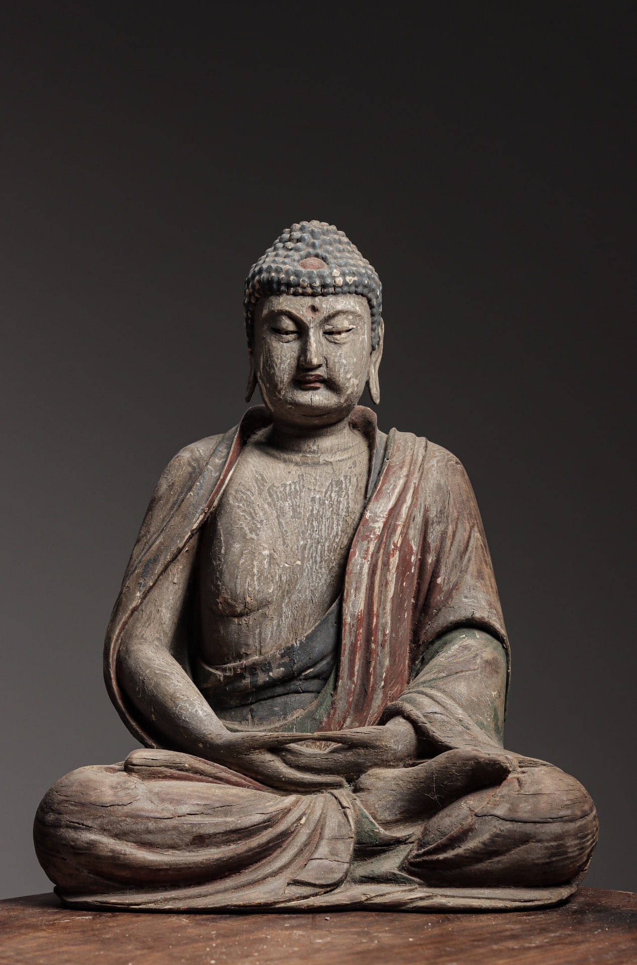 A PAINTED WOOD SEATED FIGURE OF SHAKYAMUNI BUDDHA, MING DYNASTY: 16.54" x 12.6" x 8.66" (42cm x 32cm x 22cm)A Ming Dynasty (1368-1644) painted wood Shakyamuni Buddha. Serene face, downcast eyes, dhyana mudra, flowing robes, full lotus posture. Fine carving, natural