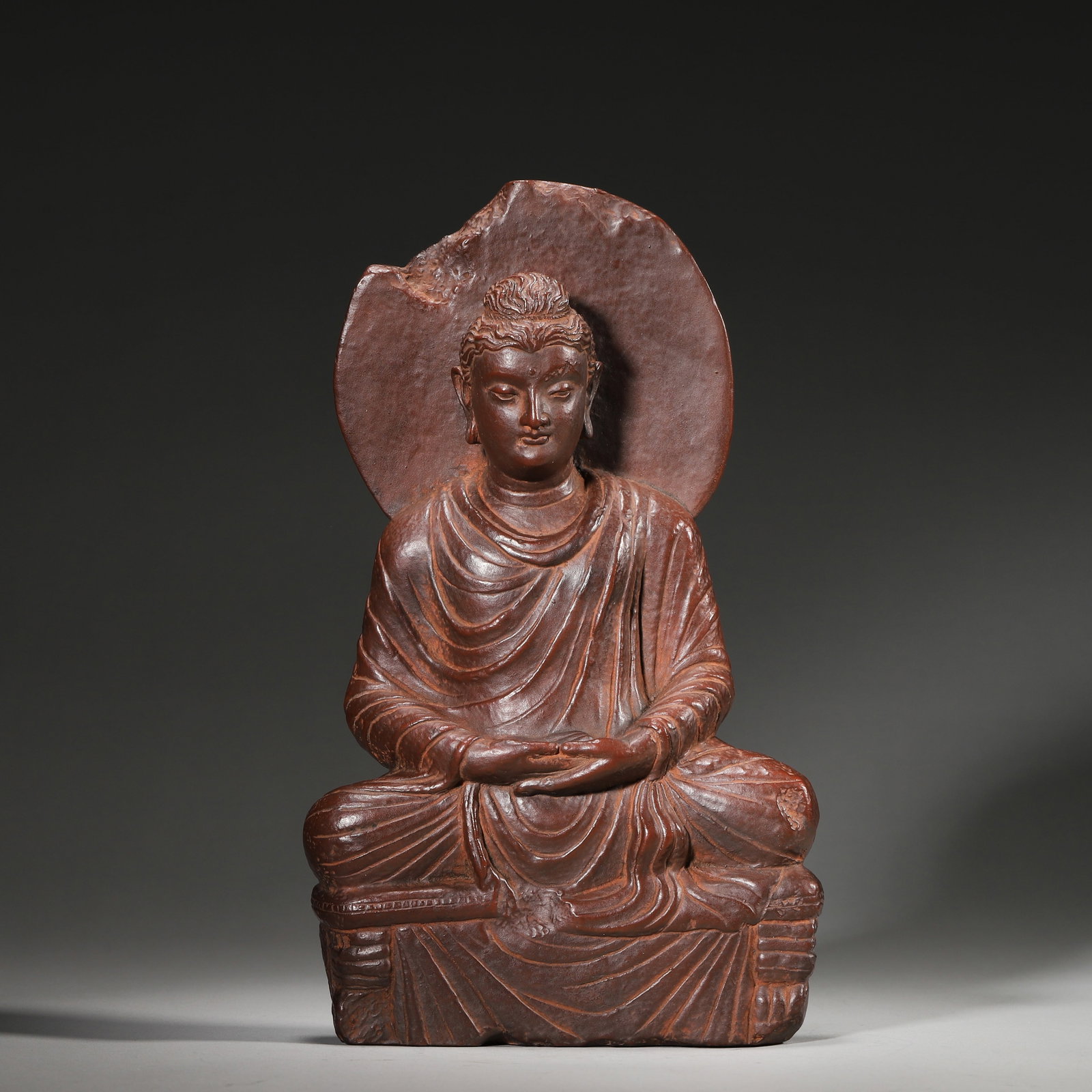 A RED POTTERY SEATED BUDDHA IN DHYANA MUDRA, GANDHARA PERIOD: L: 14cm (5.51in) W: 5cm (1.97in) H: 26cm (10.24in) Weight: 1582g (3.49lb)This exquisite red pottery seated Buddha from the Gandhara Period, in Dhyana Mudra, embodies the iconic Greco-Buddhist art styl