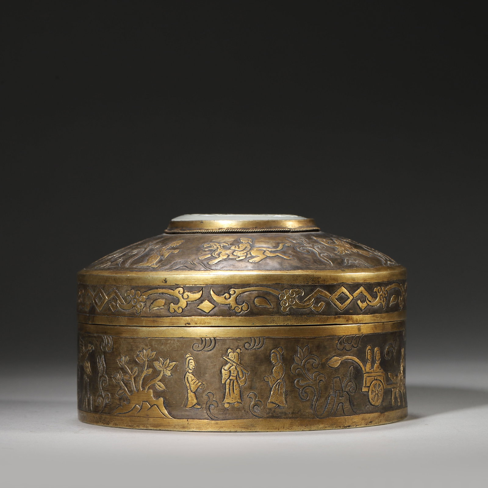 A GILT-BRONZE BOX WITH INLAID WHITE JADE OPENWORK PHOENIX PLAQUE, QING DYNASTY: Diameter: 13cm (5.12in) H: 8cm (3.15in) Weight: 652g (1.44lb)This exquisite Qing Dynasty gilt-bronze box features intricate figural scenes and a rare inlaid white jade openwork phoenix plaque. A supre