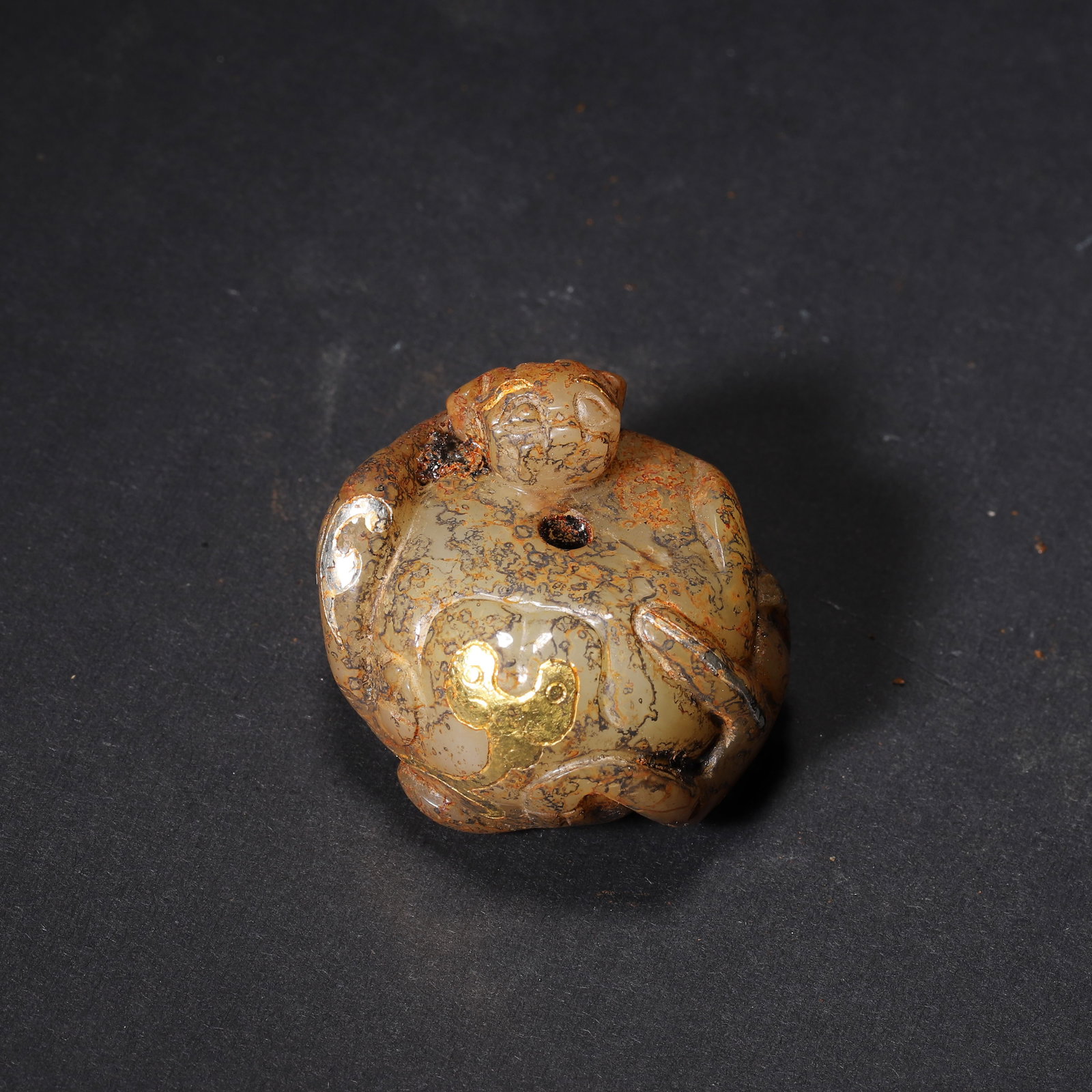 HAN DYNASTY GOLD AND SILVER INLAID JADE AUSPICIOUS BEAST WEIGHT/PENDANT: 1.42" x 1.1" (3.6cm x 2.8cm) 0.093lb (42g)This Han Dynasty jade beast, carved from Hetian jade, features gold-silver inlaid cloud patterns. Its recumbent form and natural soil patina reflect Han noble