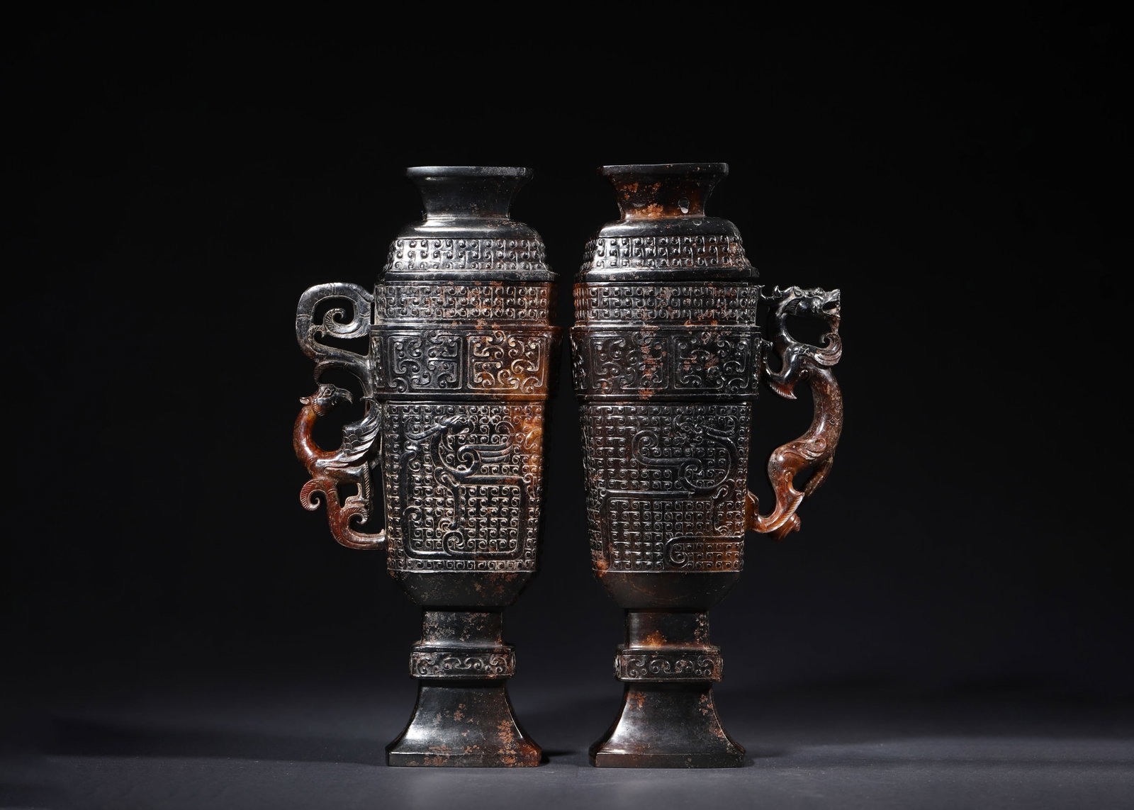 PAIR OF HAN DYNASTY HETIAN JADE COVERED CUPS WITH DRAGON AND PHOENIX HANDLES: 4.72" x 2.76" x 10.63" (12cm x 7cm x 27cm) 4.92lb (2230g)Crafted from fine Hetian jade, this pair of Han Dynasty covered cups features mercury and earth patina. Adorned with cloud and dragon patterns,
