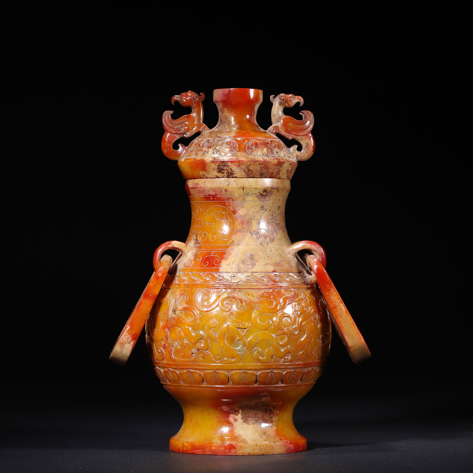 HAN DYNASTY HETIAN JADE LIDDED HU VASE WITH PHOENIX FINIAL AND HUNTING SCENE: 4.33" x 8.66" (11cm x 22cm) 2.91lb (1318g)Carved from a single block of Hetian jade, this Han Dynasty vase features a phoenix finial, movable ring handles, and vivid hunting scene reliefs. Its warm ru