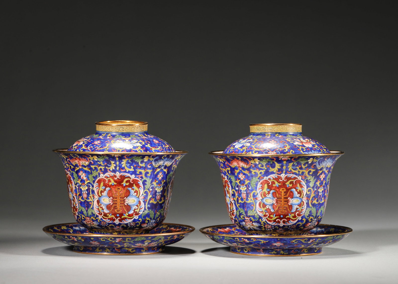 PAIR OF QIANLONG PERIOD, QING DYNASTY COPPER-BODIED ENAMEL GAIWAN WITH LONGEVITY AND FLORAL MOTIFS: 3.94in (10.0cm), 1.327lb (602.0g)A fine pair of Qianlong period copper enamel gaiwan sets with deep blue ground, vibrant floral, bat and longevity character motifs, and gilt rims. Marked "Qianlong Nia