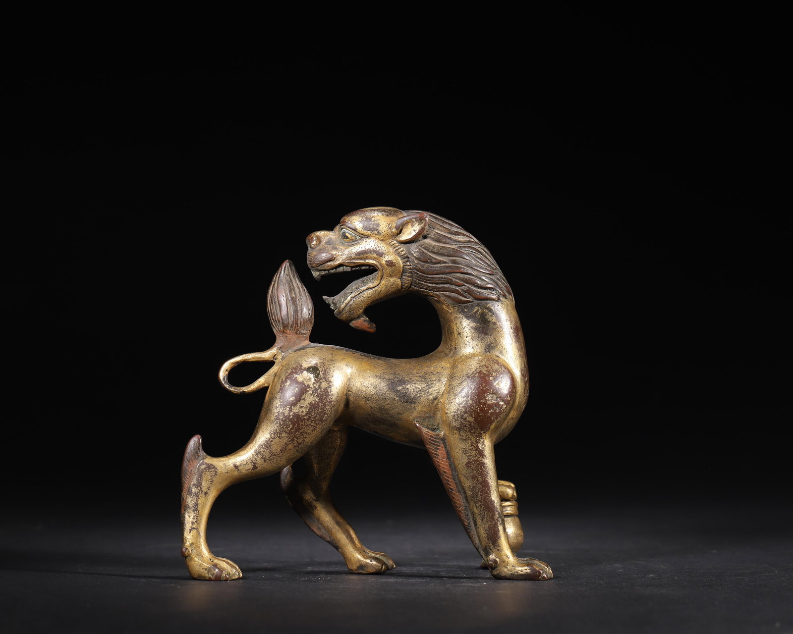 MING DYNASTY GILT-BRONZE AUSPICIOUS BEAST TREADING ON TREASURE VASE ORNAMENT: 5.12 x 2.36 x 5.51 in (13 x 6 x 14 cm), 1.55 lbs (704 g)A fine Ming Dynasty gilt-bronze auspicious beast ornament, with a dynamic turning-back pose and copper-inlaid details. Standing on a treasure va
