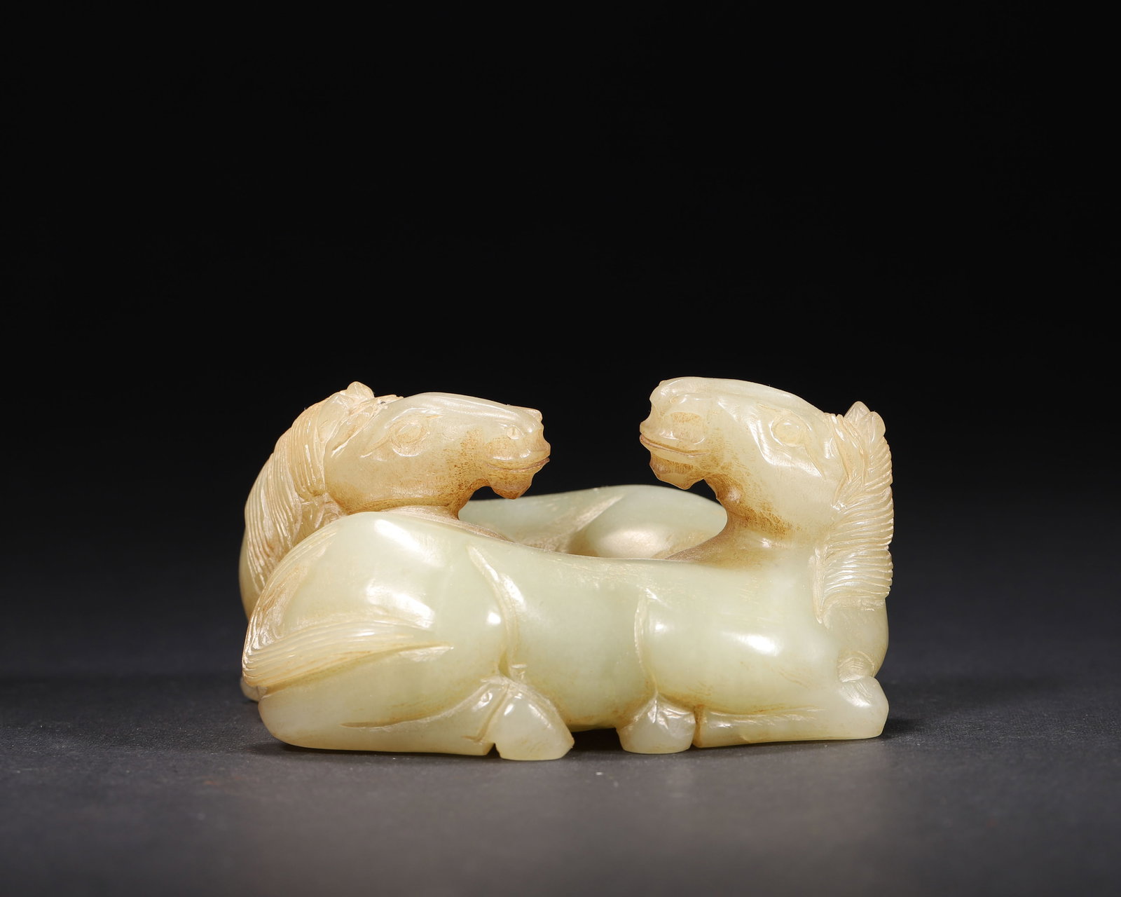 A FINE HETIAN GREEN JADE CARVING OF TWO RECUMBENT HORSES, MING DYNASTY: 3.35in x 3.15in x 1.77in (8.5cm x 8.0cm x 4.5cm), 0.787lb (357.0g)This robust Ming Dynasty Hetian green jade carving depicts two recumbent horses nuzzling, with natural earthy inclusions. Its powerful