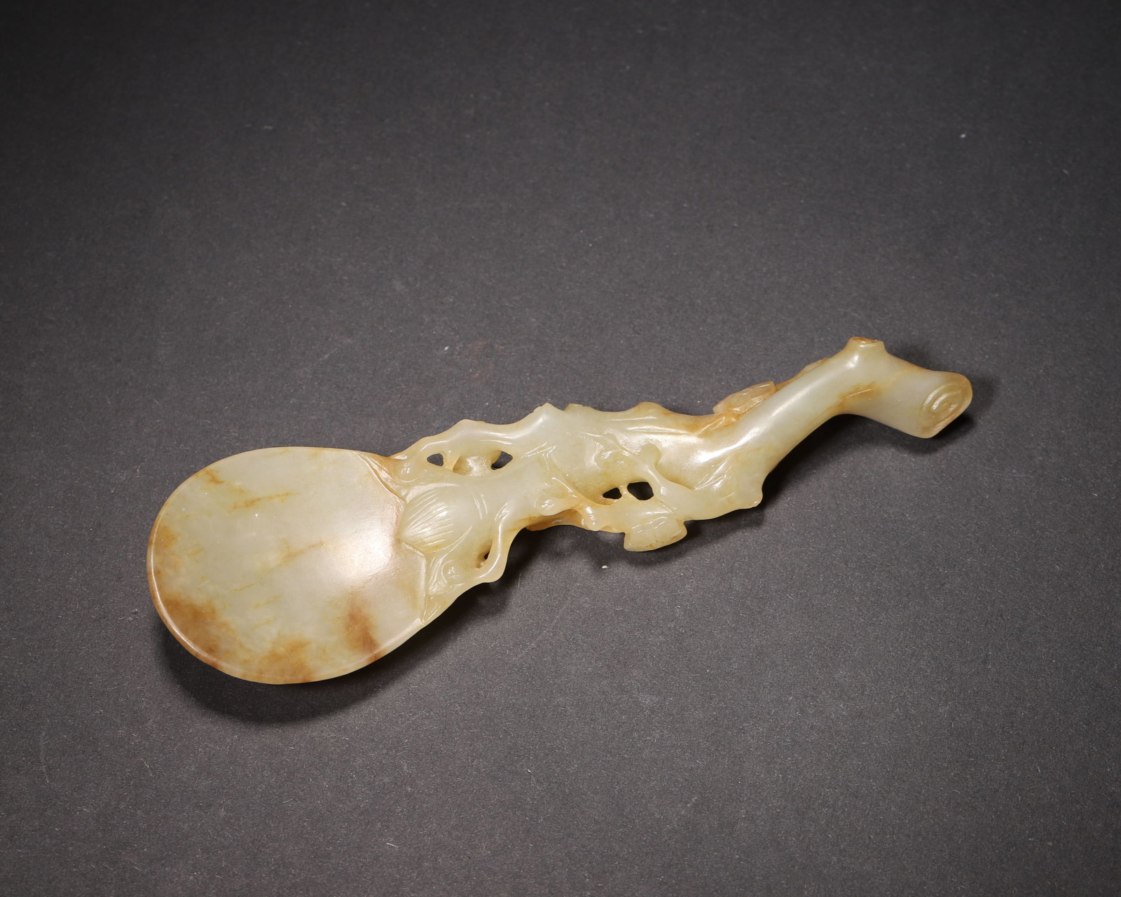 A FINE HETIAN GREENISH WHITE JADE TEA SPOON WITH PLUM BRANCH MOTIF, MID-QING DYNASTY: 4.72in x 1.38in (12.0cm x 3.5cm), 0.112lb (51.0g)This elegant Mid-Qing Hetian greenish white jade tea spoon features a plum branch handle with openwork carving and natural russet inclusions. Its delic