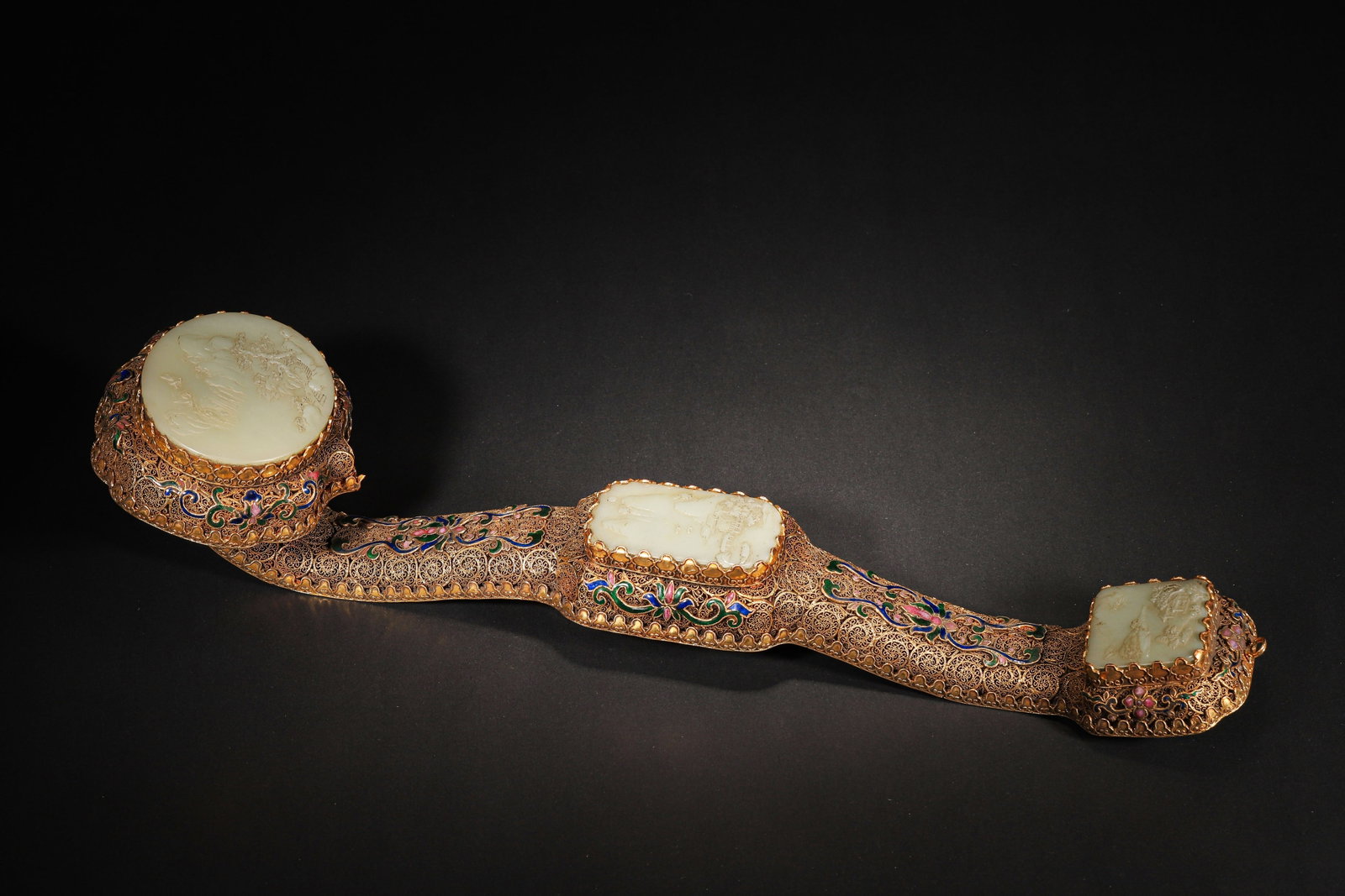 A FINE IMPERIAL GILT-SILVER FILIGREE AND ENAMEL RUYI SCEPTRE WITH INLAID CELADON JADE PANELS,: 17.72in x 4.53in (45.0cm x 11.5cm), 2.037lb (924.0g)This imperial ruyi sceptre, crafted in the Qianlong period, features gilt-silver filigree, enamel, and three celadon jade panels carved with landsca
