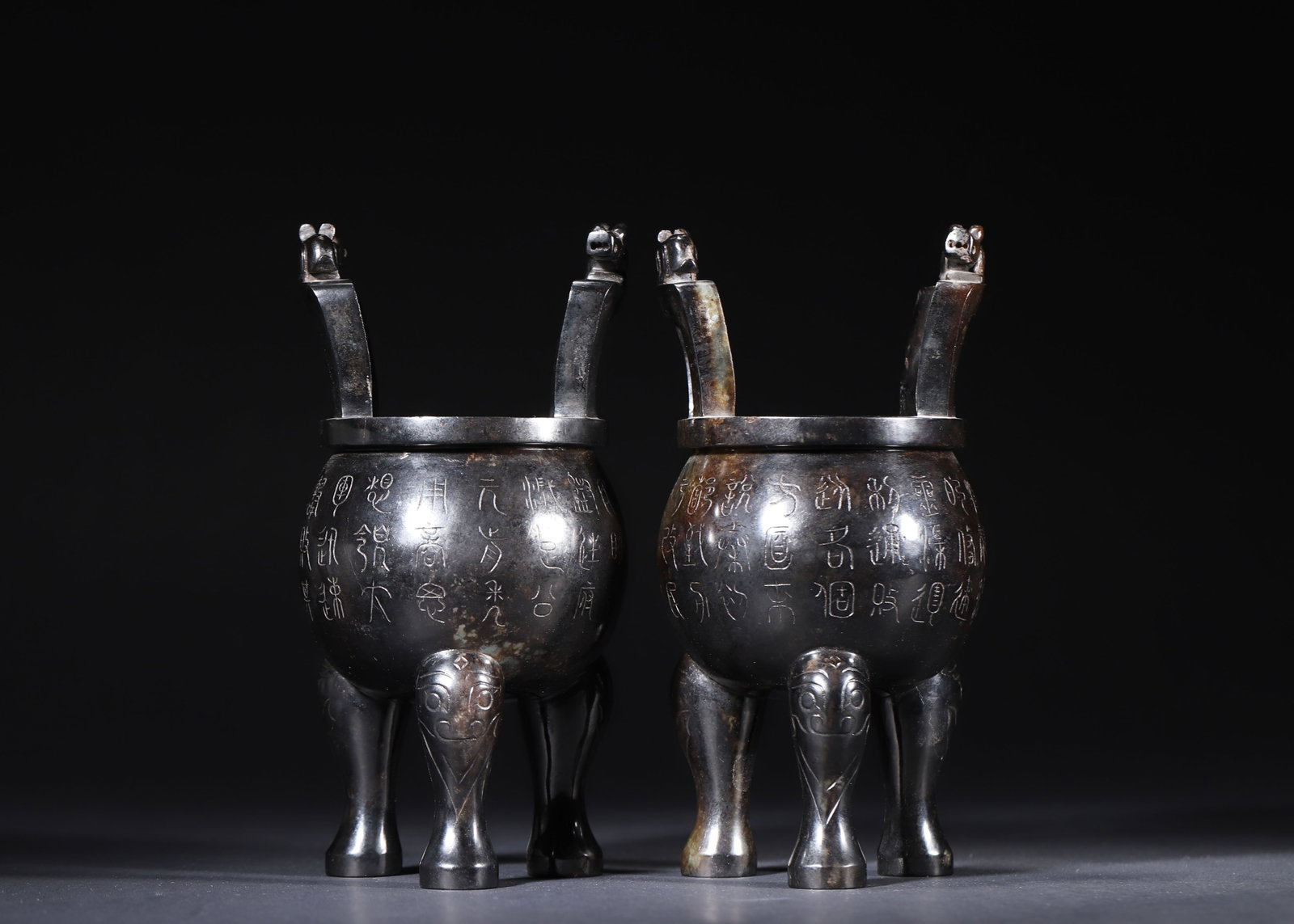 PAIR OF HAN DYNASTY HETIAN JADE TRIPOD DING VESSELS WITH BEAST HANDLES AND INSCRIPTIONS: 3.94" x 7.87" (10cm x 20cm) 3.1lb (1408g)Carved from fine Hetian jade, this pair of Han Dynasty tripods features beast-head finials, animal-faced legs, and delicate seal-script inscriptions. Their dee