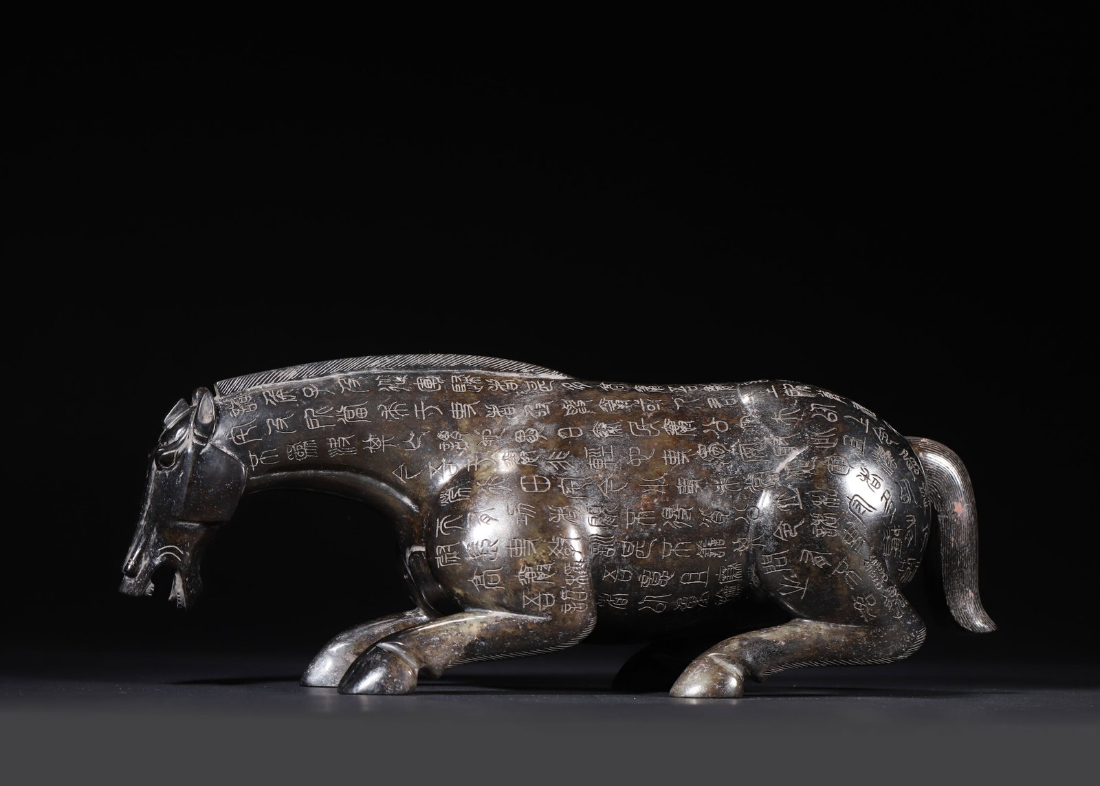 HAN DYNASTY HETIAN JADE RECUMBENT HORSE WITH INSCRIPTIONS AND MERCURY PATINA: 12.99" x 3.15" x 4.72" (33cm x 8cm x 12cm) 8.31lb (3771g)Carved from Hetian dark jade, this Han Dynasty recumbent horse features robust musculature and delicate incised seal-script inscriptions. Its d