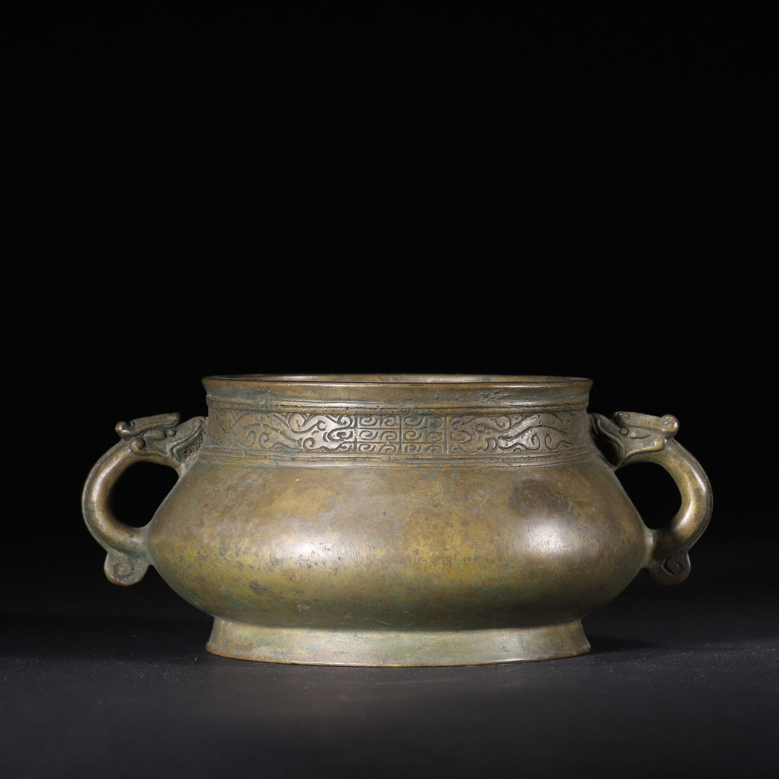 MING DYNASTY BRONZE CENSER WITH DRAGON HANDLES AND KUI DRAGON BAND: 5.91" x 2.76" (15.0cm x 7.0cm) 2.167lb (983g)This stately Ming Dynasty bronze censer features robust dragon-head handles and a finely incised kui dragon band. Its aged greenish-brown patina and privat