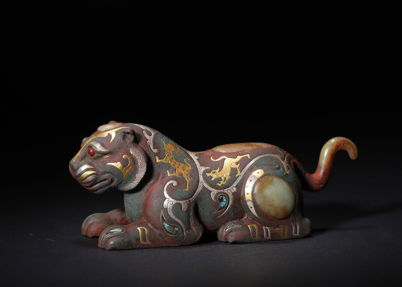 WARRING STATES TO HAN DYNASTY GOLD AND SILVER INLAID BRONZE TIGER MAT WEIGHT WITH JADE AND GEM INLAY: 7.09" x 2.36" x 2.76" (18.0cm x 6.0cm x 7.0cm) 1.338lb (607g)This Warring States to Han Dynasty bronze tiger mat weight features gold-silver inlaid patterns, jade and gem inlays. Its crouching form an