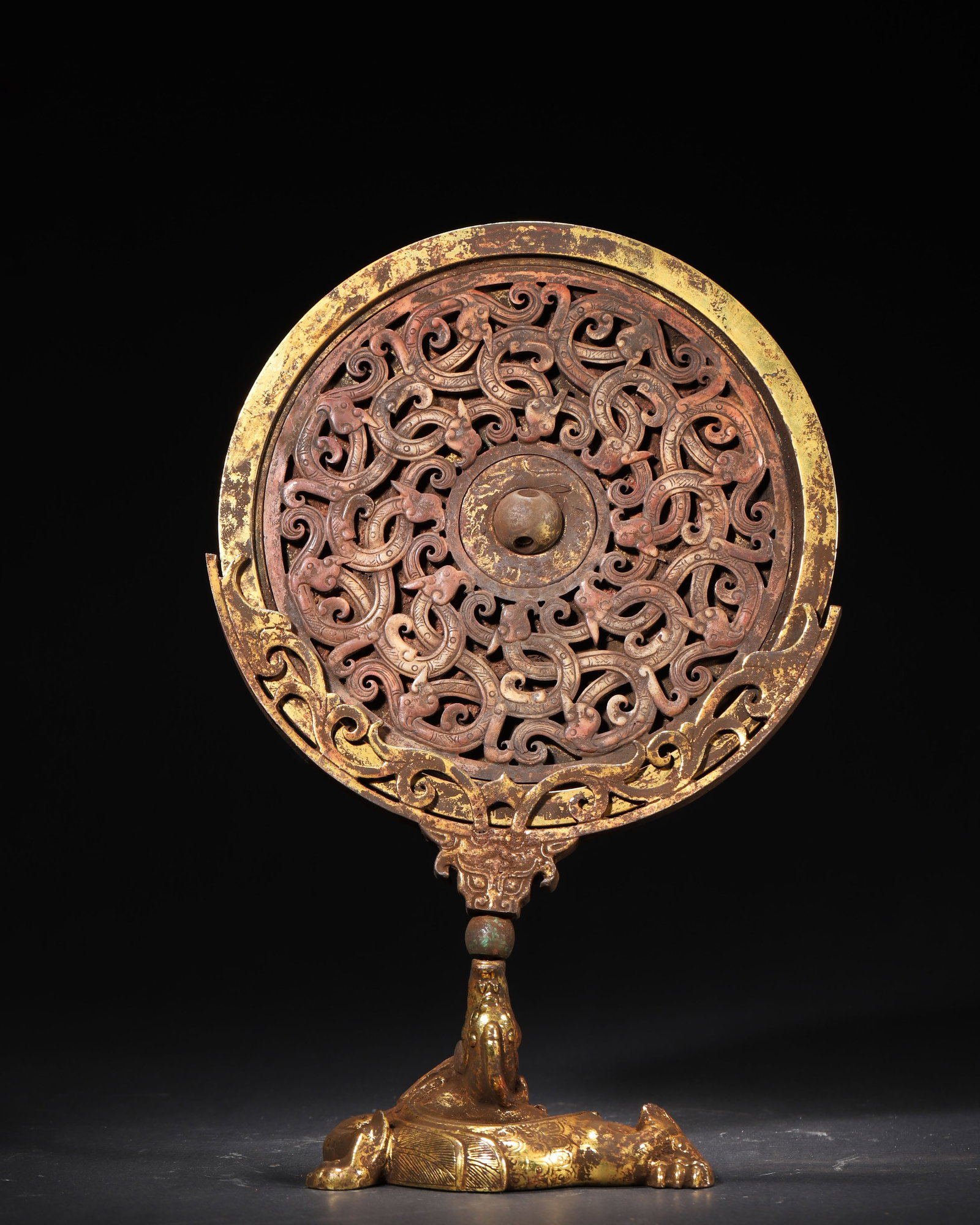 A FINE HAN DYNASTY GILT-BRONZE OPENWORK 'PAN CHI' MIRROR WITH BEAST BASE: 28x18cm (11.02x7.09in)This Han Dynasty gilt-bronze mirror features intricate openwork 'Pan Chi' dragon patterns and a recumbent beast base. Gilded throughout, it exemplifies the exquisite craftsmanshi