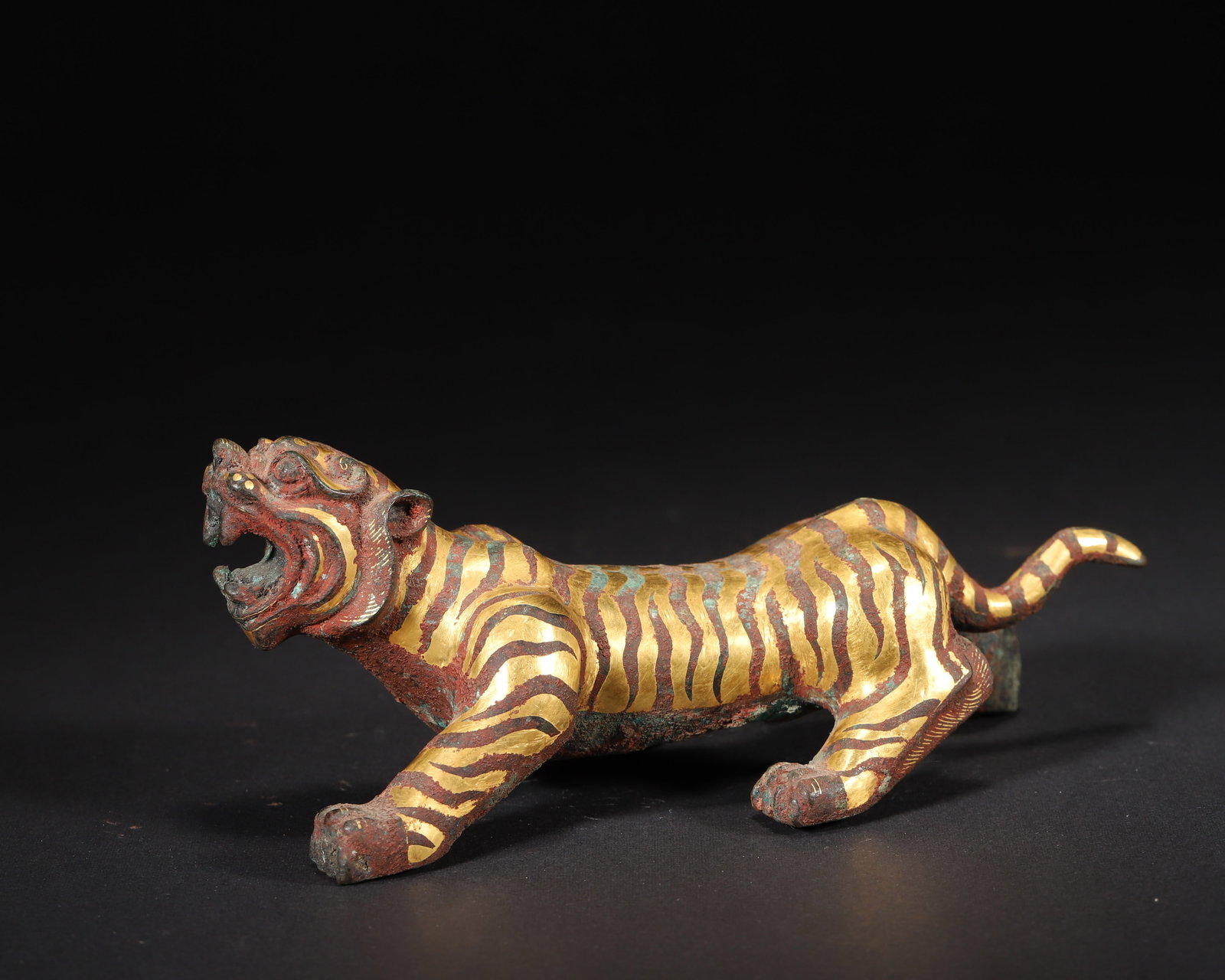 WESTERN HAN DYNASTY GOLD-INLAID BRONZE TIGER PAPERWEIGHT: 6.3in x 3.15in x 2.36in (16.0cm x 8.0cm x 6.0cm), 0.935lb (424.0g)This Western Han tiger paperweight, crafted in bronze with gold-inlaid stripes, captures a roaring, prowling pose. Its vivid detailing