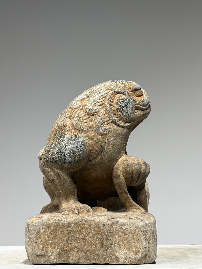 Bluestone Crouching Lion with Ball, Sui Dynasty: A Sui dynasty bluestone carving of a crouching lion with ball, carved from a solid stone block with an integrated square base. The guardian beast rests its front paws upon a ribbon-wrapped ball, featu