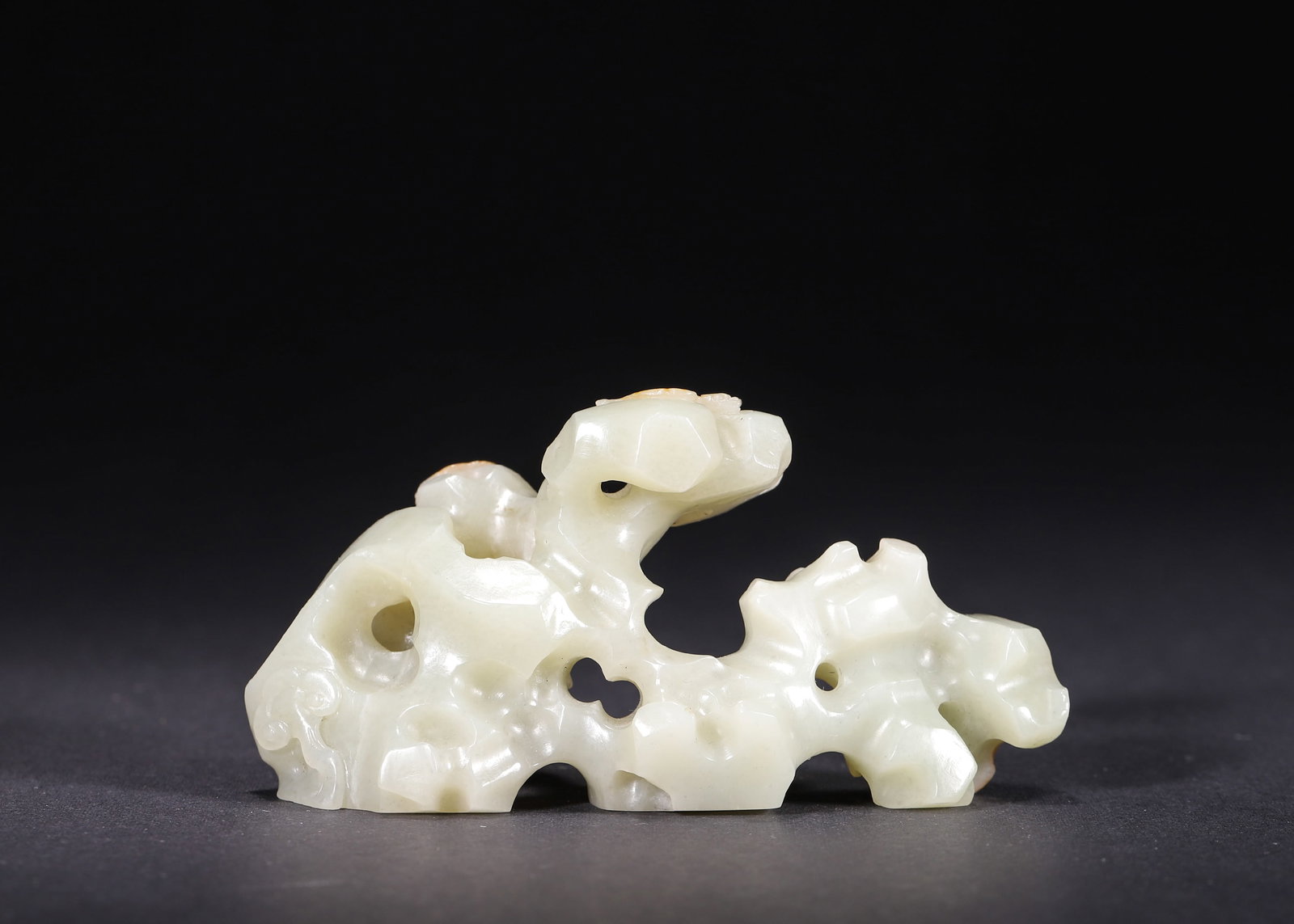 Pale Celadon Jade Brush Rest with Bat and Lingzhi Motifs, Qianlong Period, Qing Dynasty: A Qianlong period, Qing dynasty pale celadon jade brush rest, hollow carved in the form of a porous Taihu scholar’s rock. The natural russet skin is skillfully incorporated into three bats paired wi