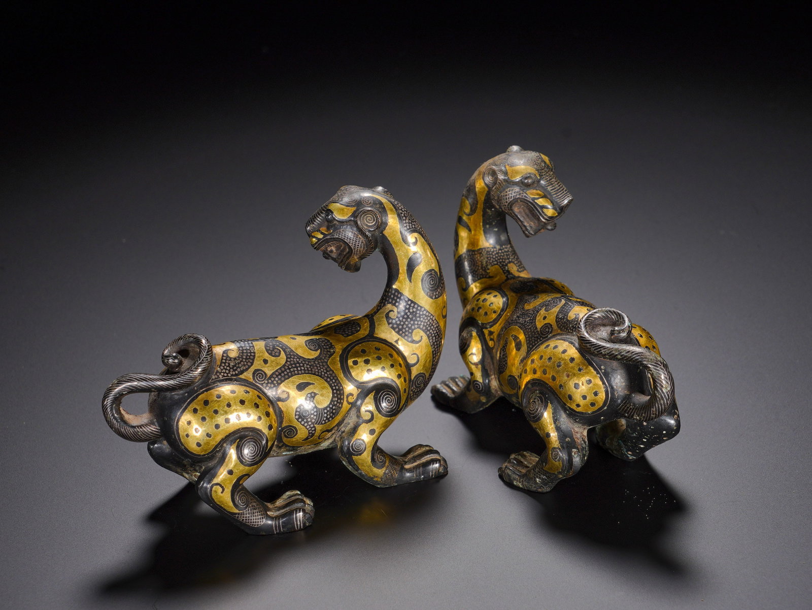 WARRING STATES PERIOD, A PAIR OF INLAID GOLD AND SILVER AUSPICIOUS BEASTS: Luxury bronze wares of this kind were exclusive to high-ranking nobles, serving as table weights or vessel supports, symbolizing supreme authority and auspiciousness. The gold-silver inlay craft was a