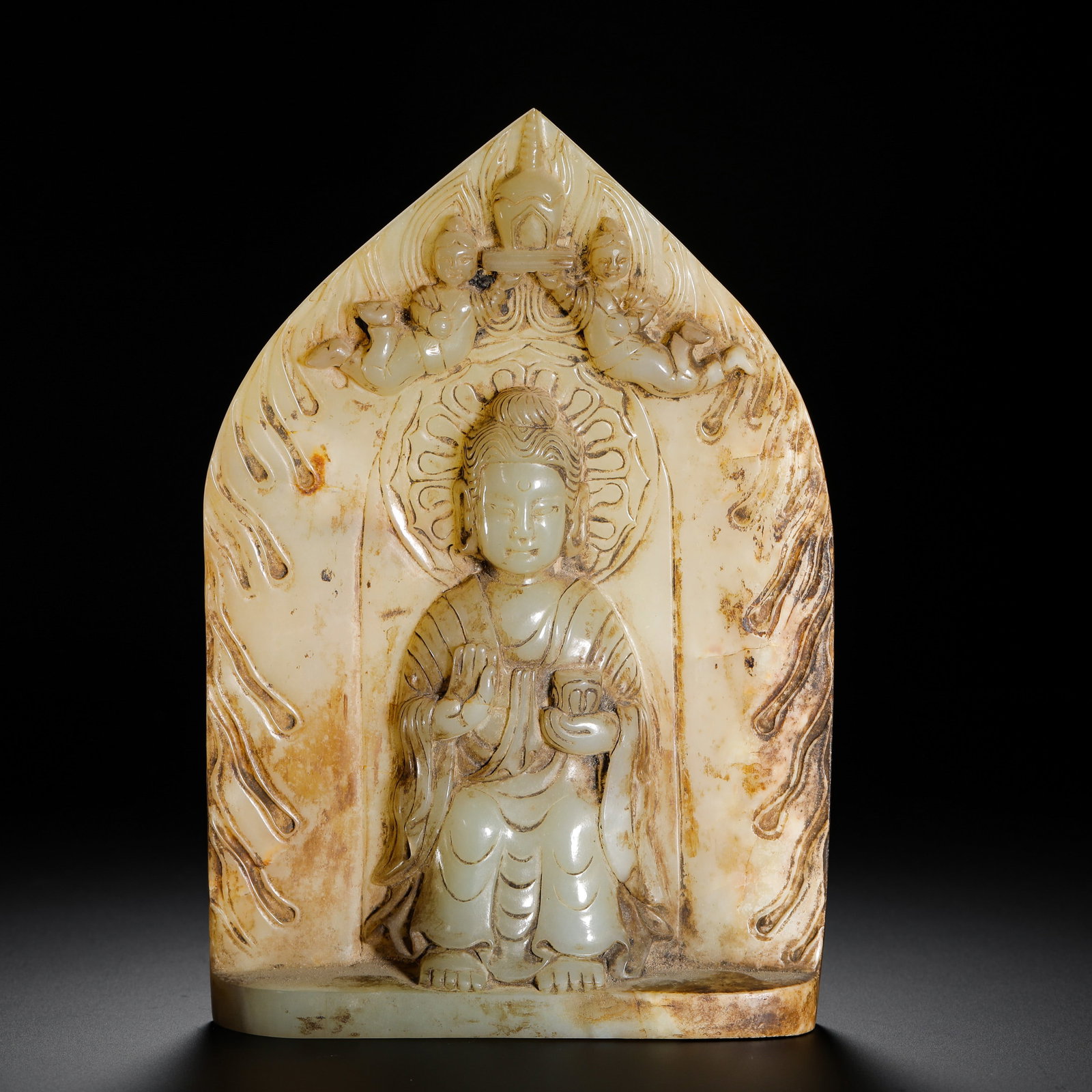 SUI-TANG HETIAN JADE BUDDHA STATUE: Sui-Tang jade Buddhist plaque featuring seated Shakyamuni preaching mudra, flying apsaras holding stupa atop, flame-patterned aureole, covered in ancient soil patina, a fine medieval Buddhist jade car