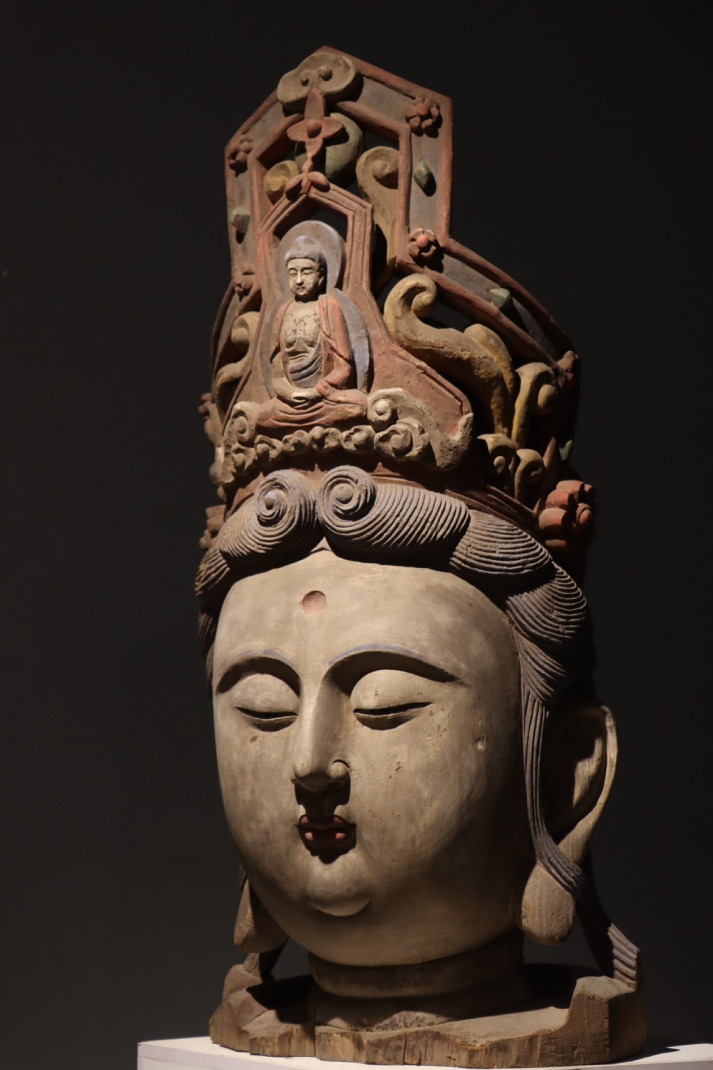 TANG DYNASTY WOODCARVING PAINTED GUANYIN HEAD: Wood-carved Guanyin head with residual ancient colored pigments. The hollow tall crown is carved with a seated Buddha at the center, surrounded by scroll grass and flower ornaments retaining red, gree