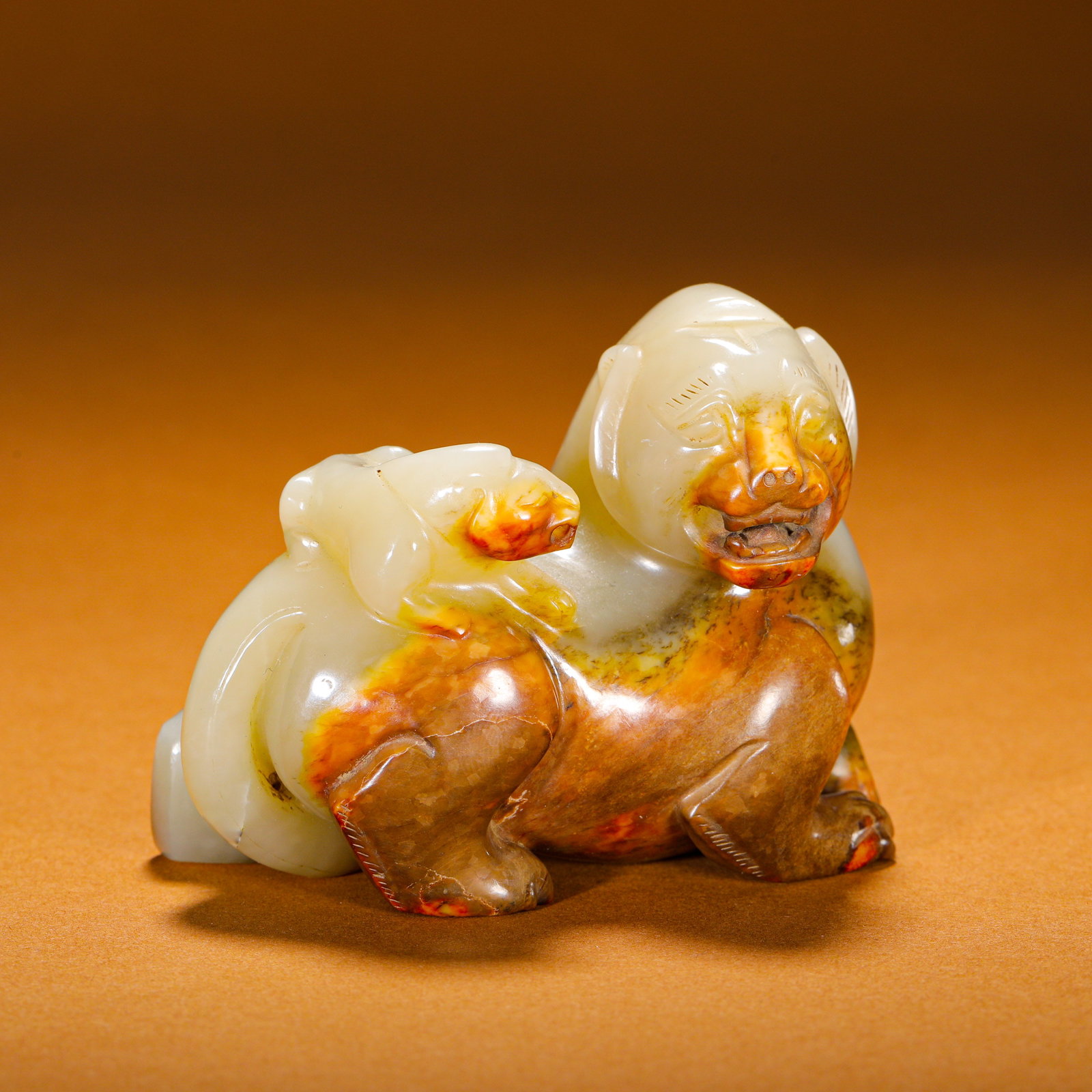 HAN DYNASTY, HETIAN WHITE JADE MOTHER-AND-CUB BEAST ORNAMENT: Round-carved white Hetian jade pendant of mother-and-cub auspicious beasts, Han Dynasty. Smooth jade with natural reserved russet skin covering the beast's muzzle and limbs. The mother beast crouches 