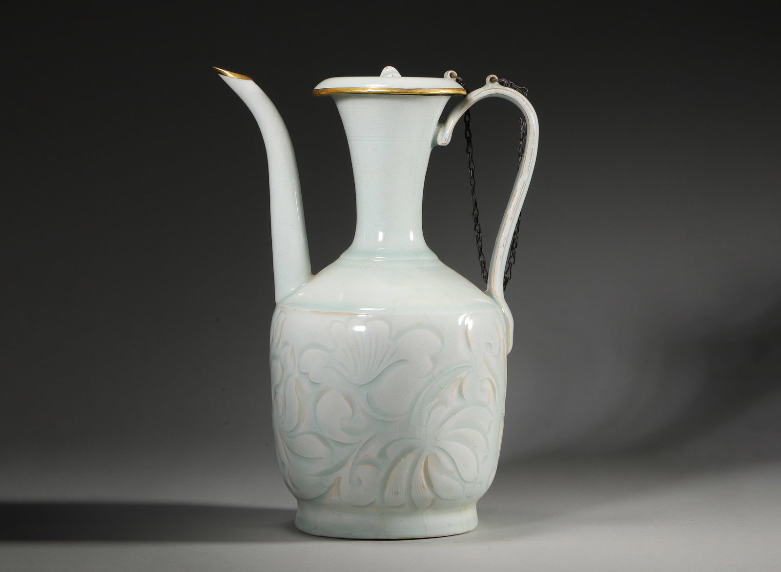 Yingqing Glazed Carved Ewer, Song Dynasty, 960-1279: Flared mouth and long neck,with curved spout,loop handle and cover. Body carved with scrolling floral motifs. Covered with pale yingqing glaze,foot ring exposed,well-proportioned form. Dimensions: Dia