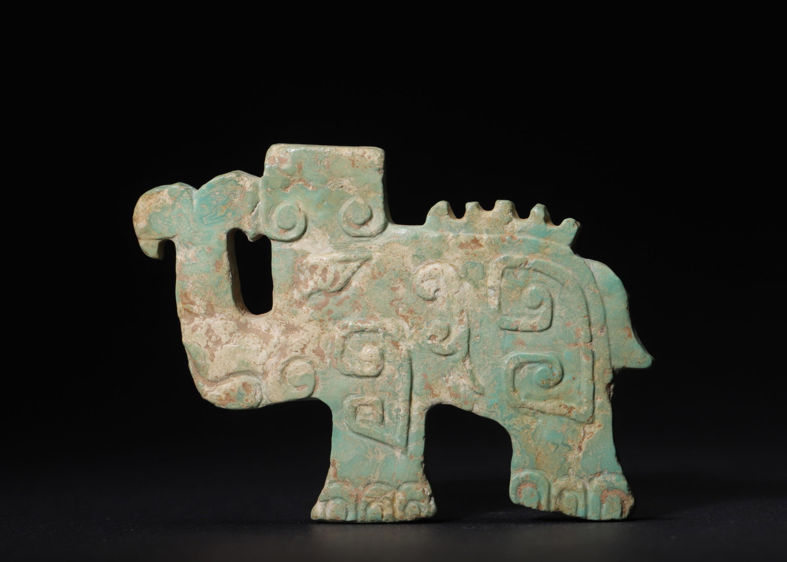 Turquoise Elephant Pendant, Shang Dynasty (1600-1046 BC): Flat carved turquoise elephant pendant, decorated on both sides. Adorned with characteristic Shang dynasty scroll and beast motifs, crest upon the back, openwork beside the trunk. Surface marked with 